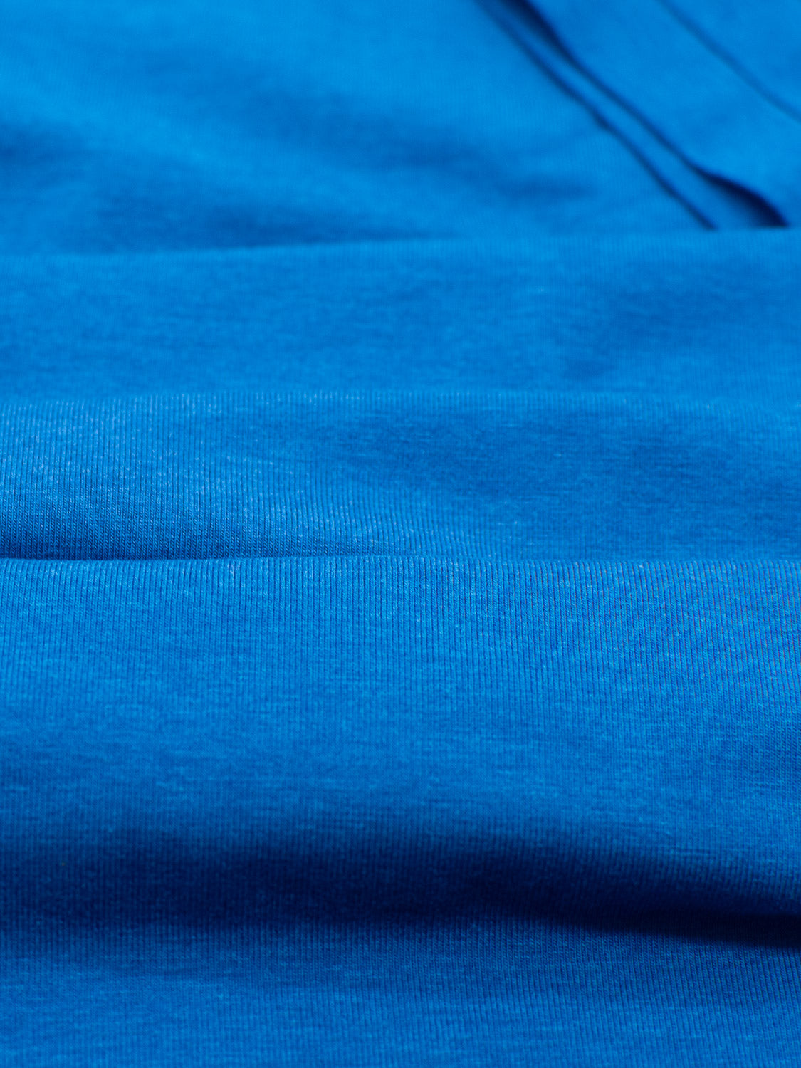 Close-up of a vibrant blue bamboo fabric from the ID Menswears Slay Wide Neck Bamboo Blend Tee. The soft, lightweight material features a smooth, subtly textured surface with gentle folds that highlight its consistent color.