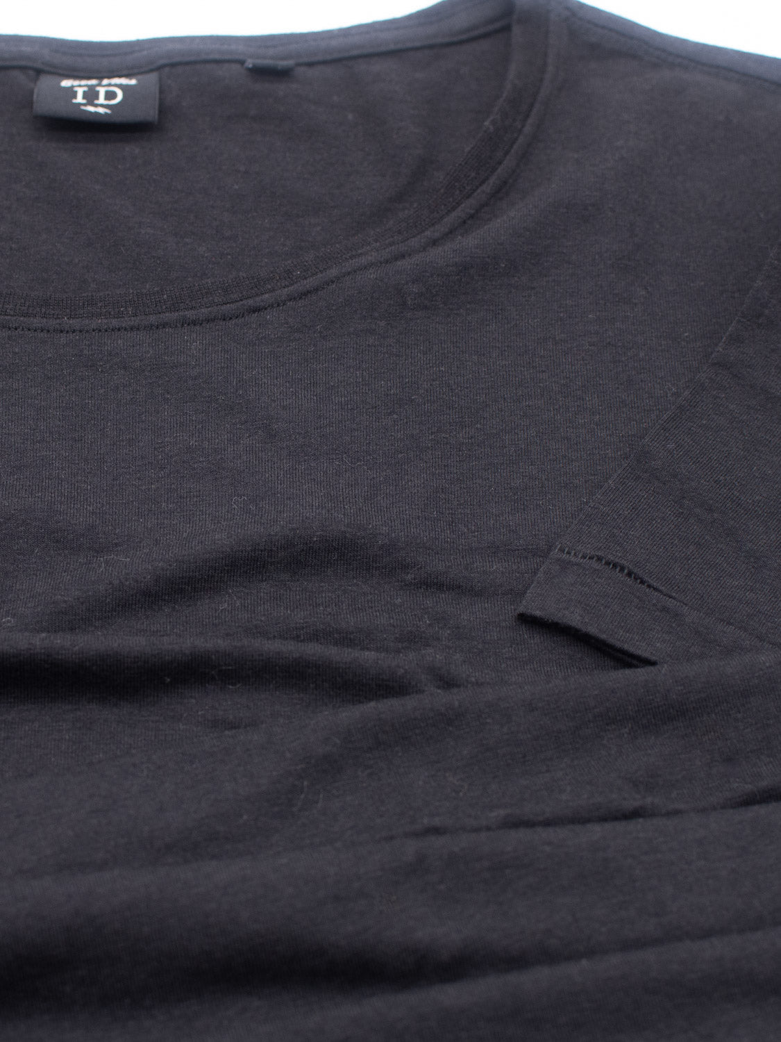 A black Slay Wide Neck Bamboo Blend Tee from ID Menswear is laid flat, highlighting the fine texture and a close-up of the tag at the collar.
