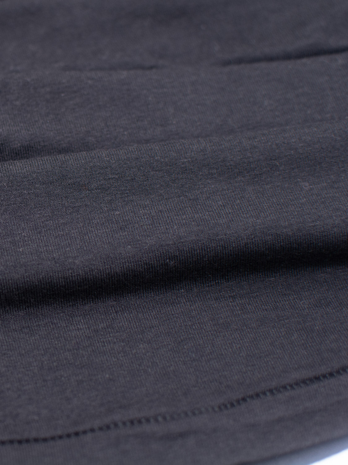 A close-up of a smooth, dark gray fabric with fine stitching along the bottom edge, this Slay Wide Neck Bamboo Blend Tee by ID Menswear features subtle horizontal lines. Crafted from organic cotton, its soft and stretchy texture resembles a premium jersey under even lighting.