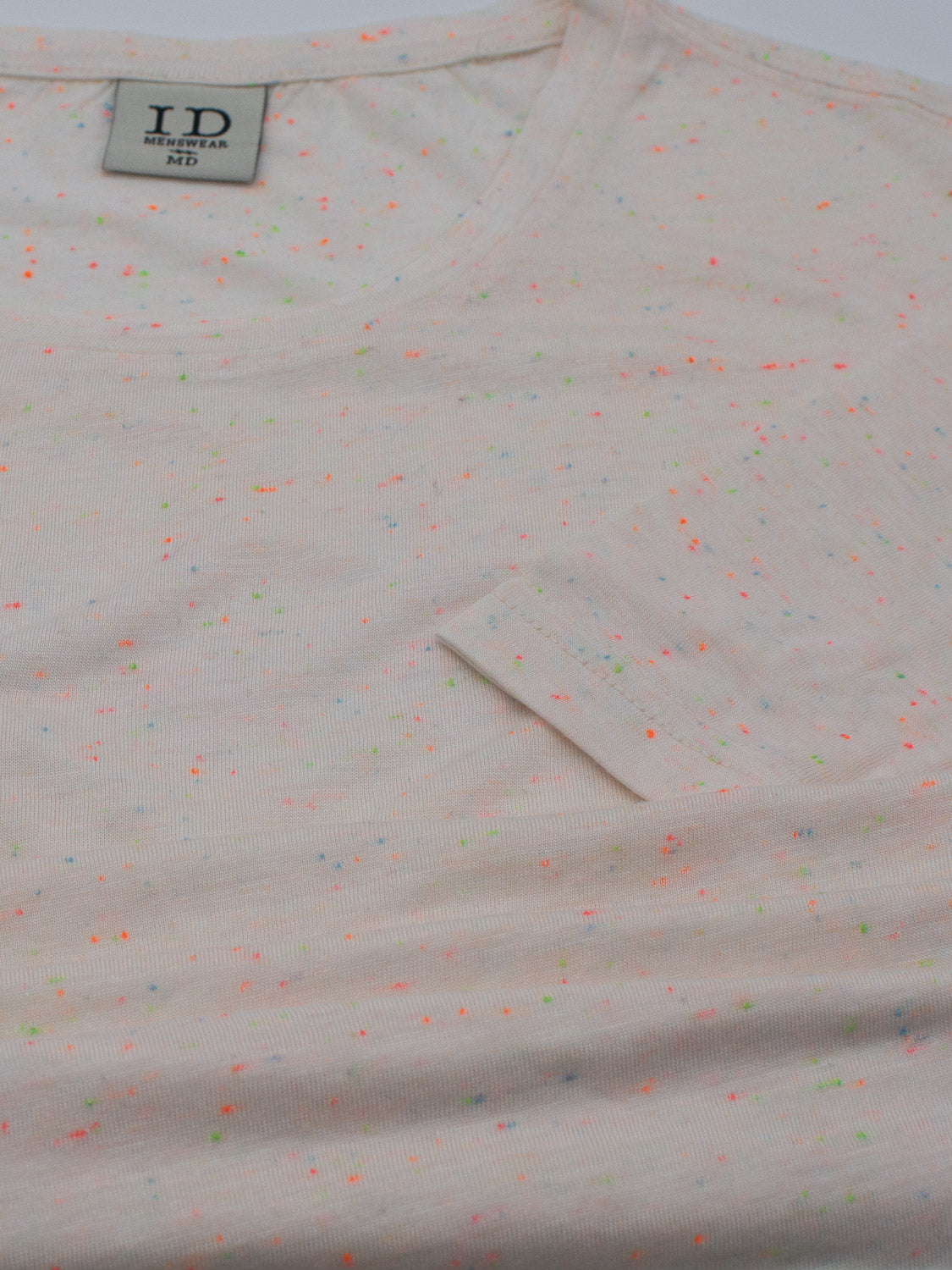 The Outclass Bamboo Neppy Tee, by ID Menswear, is a white crew neck T-shirt with neon pink, yellow, and green speckles. Made from lightweight bamboo jersey, it includes a small left chest pocket and a neckline label showing the brand ID and size M/5.