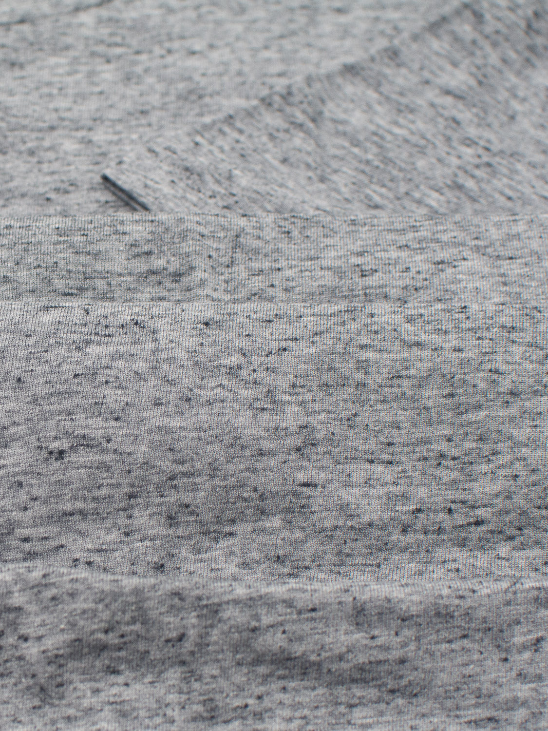 Close-up of the Outclass Speckled Crew Neck Tee by ID Menswear, showcasing its folded gray fabric with a cozy cotton/poly jersey feel, slightly textured surface, and scattered black speckles—ideal for everyday wear.