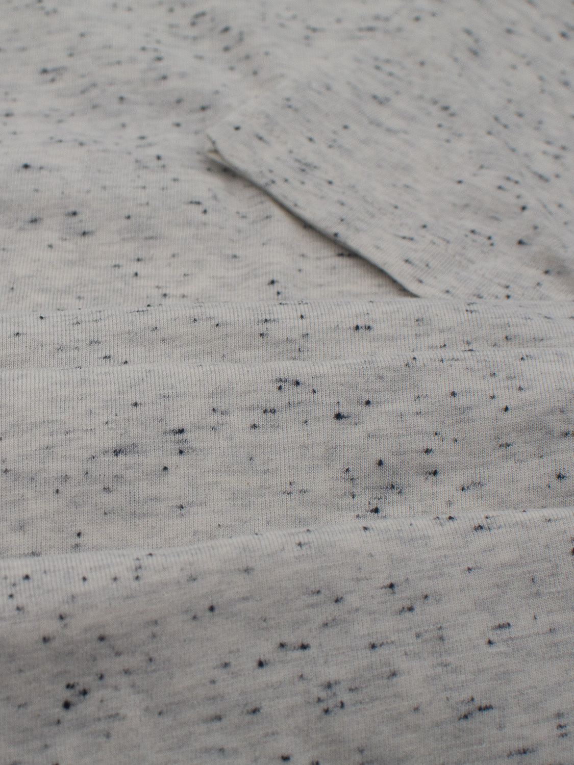 Close-up of the Outclass Speckled Crew Neck Tee by ID Menswear features a light gray speckled design. Crafted from soft, ribbed cotton/poly jersey fabric, it offers a subtle pattern perfect for daily wear.