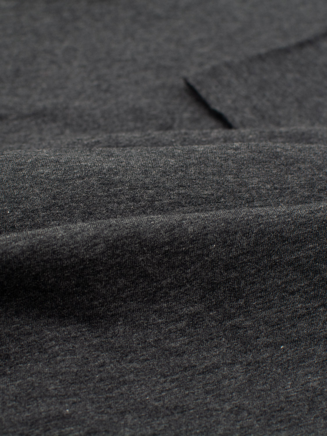 Close-up of dark gray fabric texture, highlighting its weave. This lightweight cotton jersey from ID Menswears Outclass Cotton Crew Neck Tee looks soft and smooth with delicate shading variations, perfect for creating a comfortable T-shirt or crew neck design.