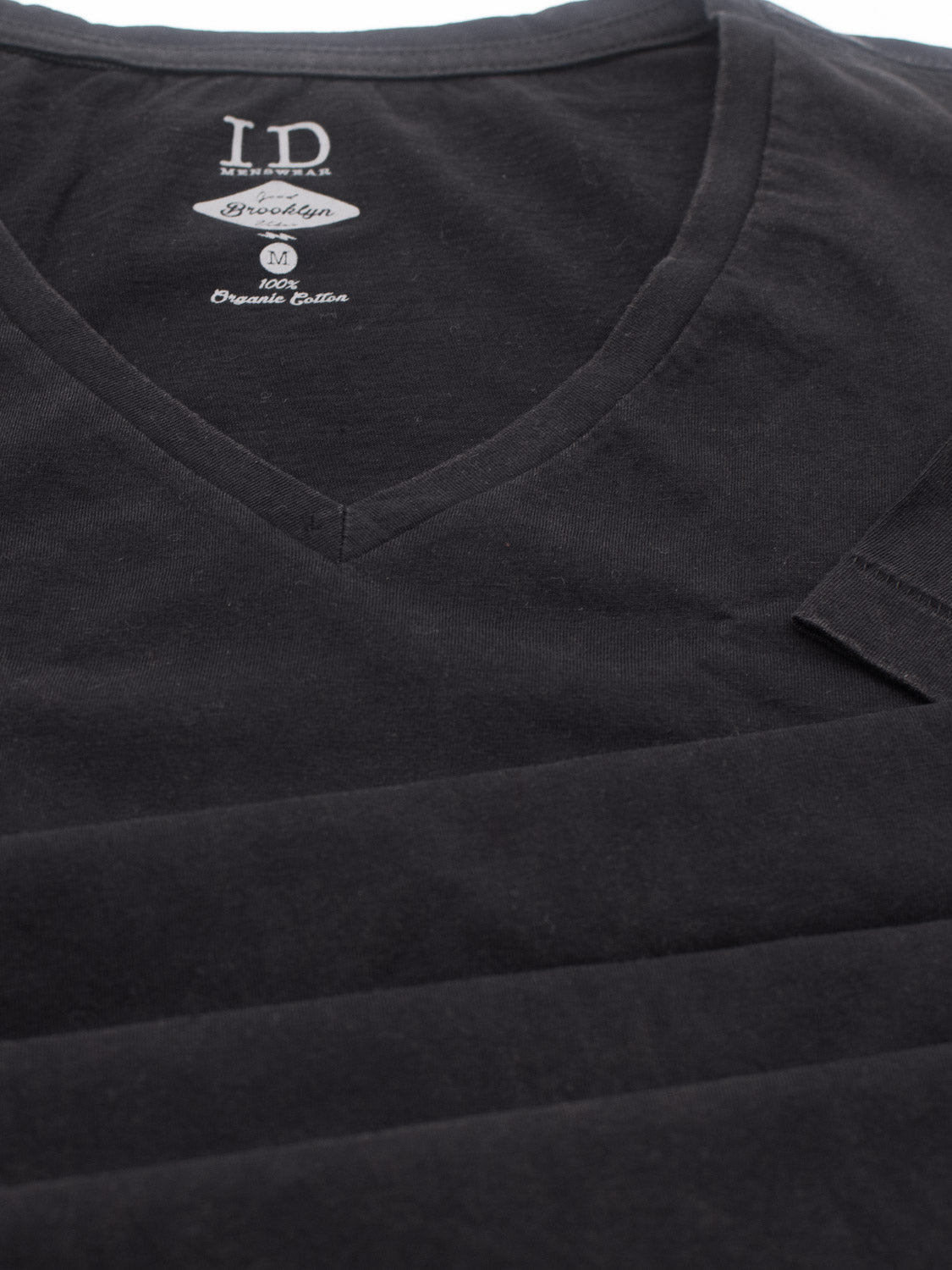 Close-up of a black V-neck t-shirt featuring the label ID Menswear, size M. Its the Legacy Organic Cotton V Neck Tee, made from 100% organic cotton. This classic fit shirt blends modern style with a vintage look, neatly folded.