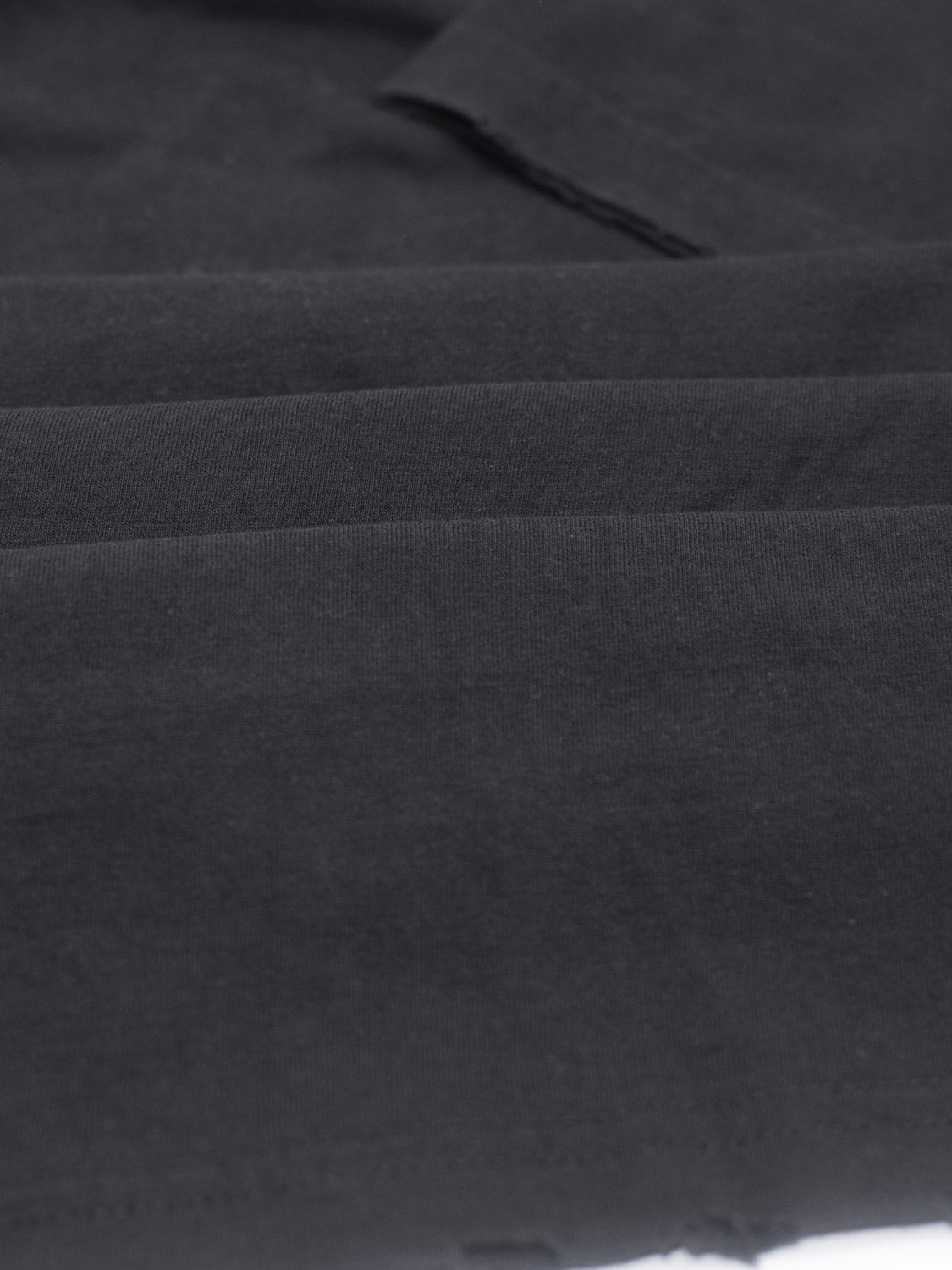 Close-up of a neatly folded Trekker Tattered Crew Neck Tee by ID Menswear, crafted from black organic cotton. The image highlights its smooth texture and precise edges, showcasing the lightweight jerseys quality.