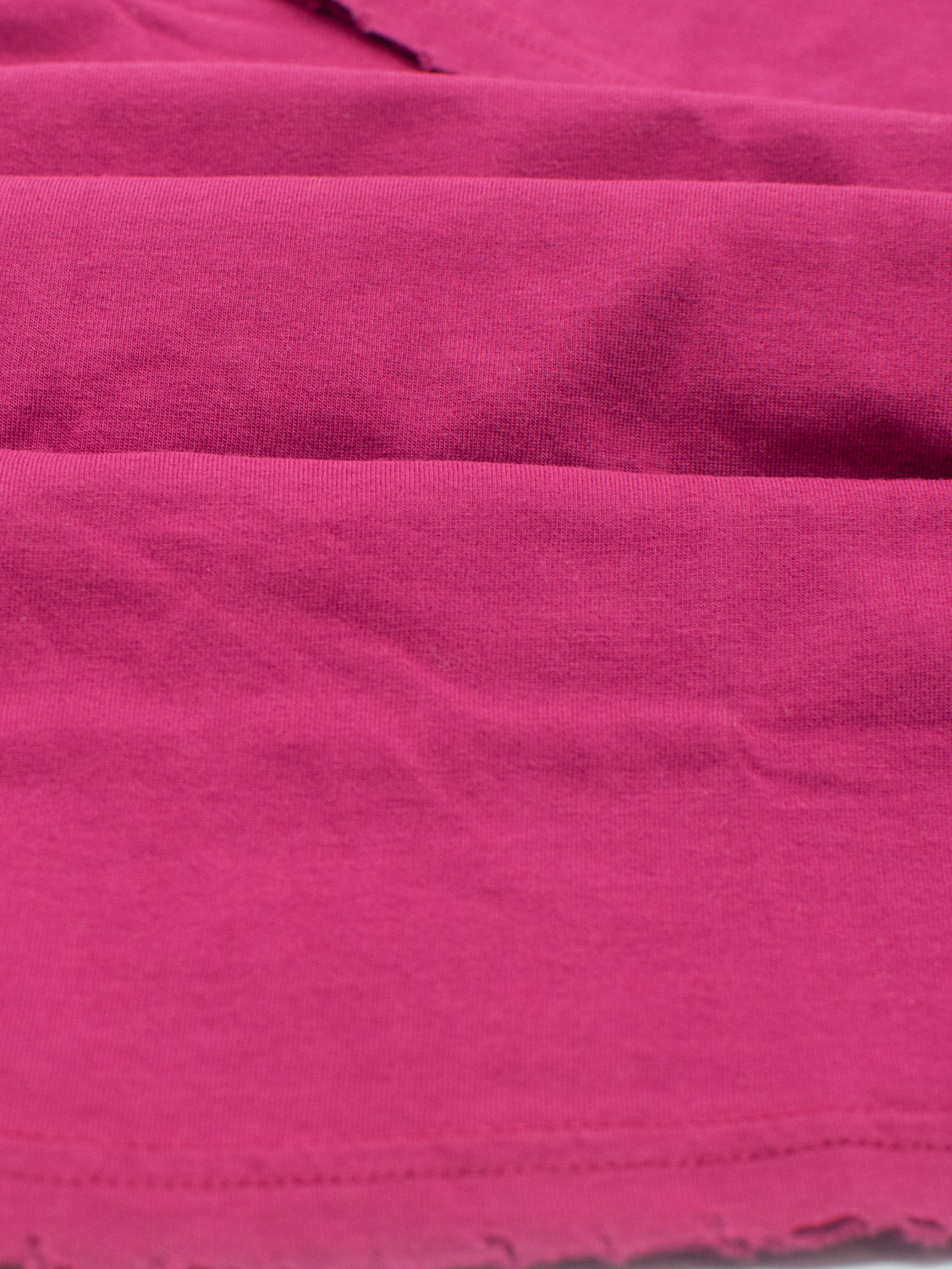Close-up of a vibrant pink organic cotton fabric with visible stitching. The lightweight jersey material appears slightly wrinkled, showcasing a smooth texture and even coloration, much like the Trekker Tattered Crew Neck Tee by ID Menswear.