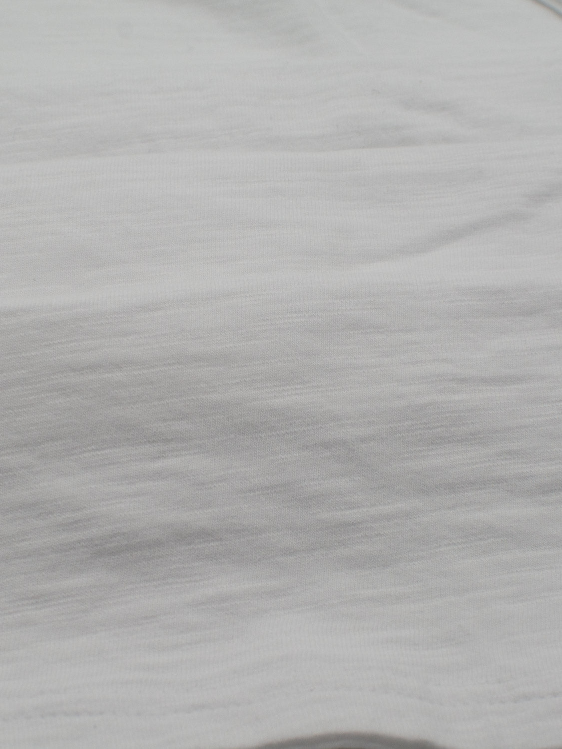 A close-up of a smooth white fabric with subtle horizontal textures, reminiscent of the casual style perfect for everyday wear, featured in the Mini Flip Slub Yarn Tee by ID Menswear.