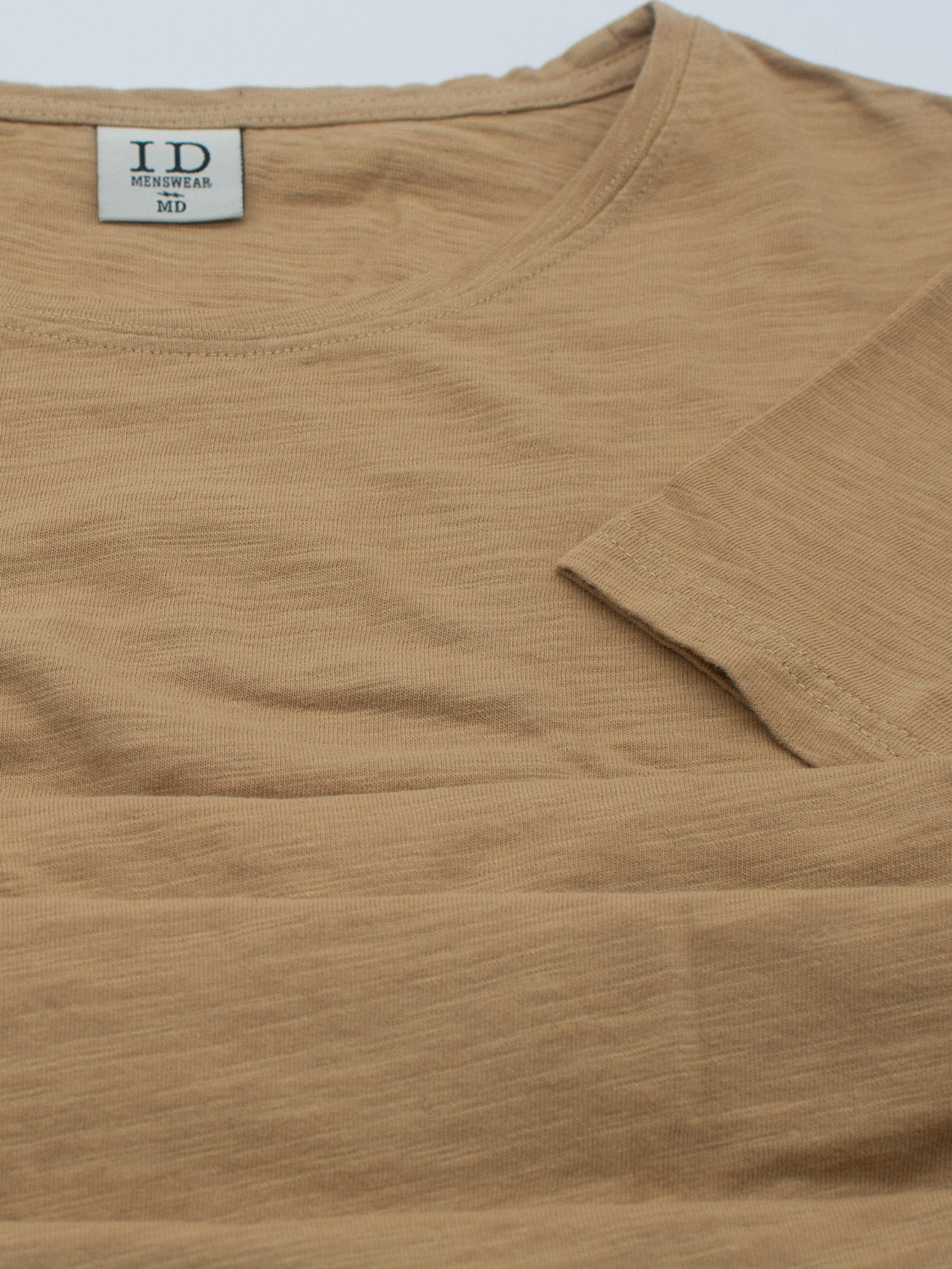 The Mini Flip Slub Yarn Tee by ID Menswear is a beige cotton T-shirt with a round neckline, featuring a small beige back neck tag with size and brand details. Its soft, lightweight fabric is ideal for everyday casual wear and laid-back occasions.