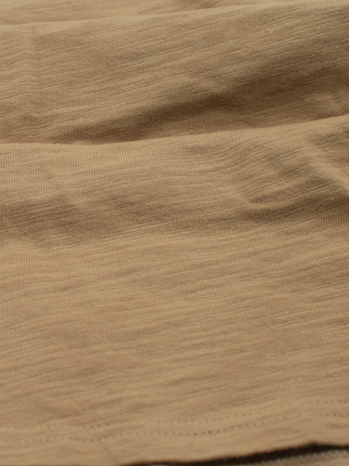 Close-up of a beige fabric with a textured, slightly wavy appearance, resembling the softness of an ID Menswear Mini Flip Slub Yarn Tee. Its subtle horizontal lines and smooth finish make it perfect for achieving a casual look reminiscent of everyday wear.