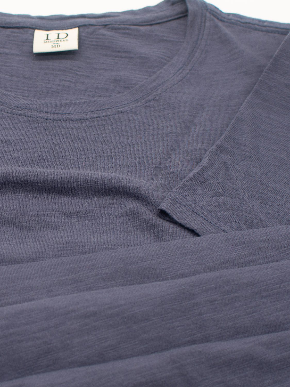 A folded dark gray Mini Flip Slub Yarn Tee by ID Menswear features a round neckline. The label shows LD and M for medium size, emphasizing its soft, lightweight fabric, perfect for everyday casual wear.