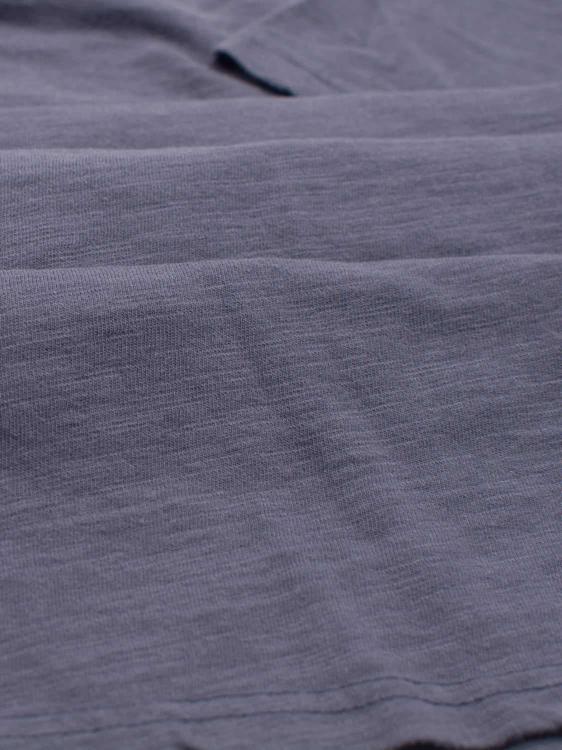 Close-up of the gray, textured fabric of the Mini Flip Slub Yarn Tee by ID Menswear. Its slightly wrinkled surface with horizontal lines and subtle shade variations is perfect for everyday wear or a relaxed casual look.