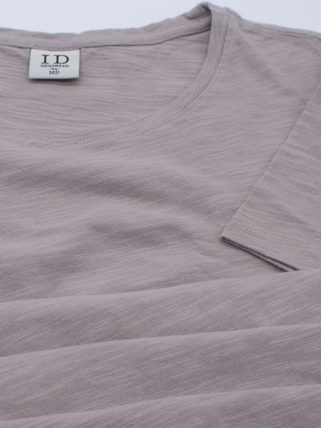A close-up of a light gray Mini Flip Slub Yarn Tee by ID Menswear showcases its round neckline and subtle texture. The visible clothing label reads ID, subtly enhancing its casual appeal, while one sleeve is partially visible, making it perfect for everyday wear.