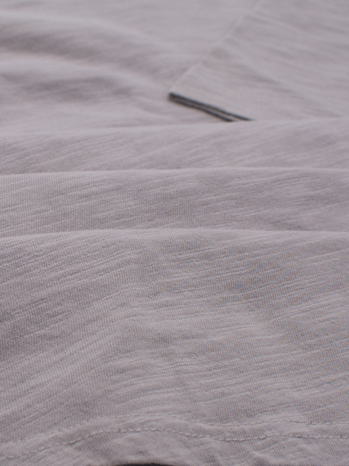 Close-up of a light gray folded fabric with texture and seams, perfect for ID Menswears everyday Mini Flip Slub Yarn Tee. The materials subtle sheen and slightly wrinkled look add to its casual charm.