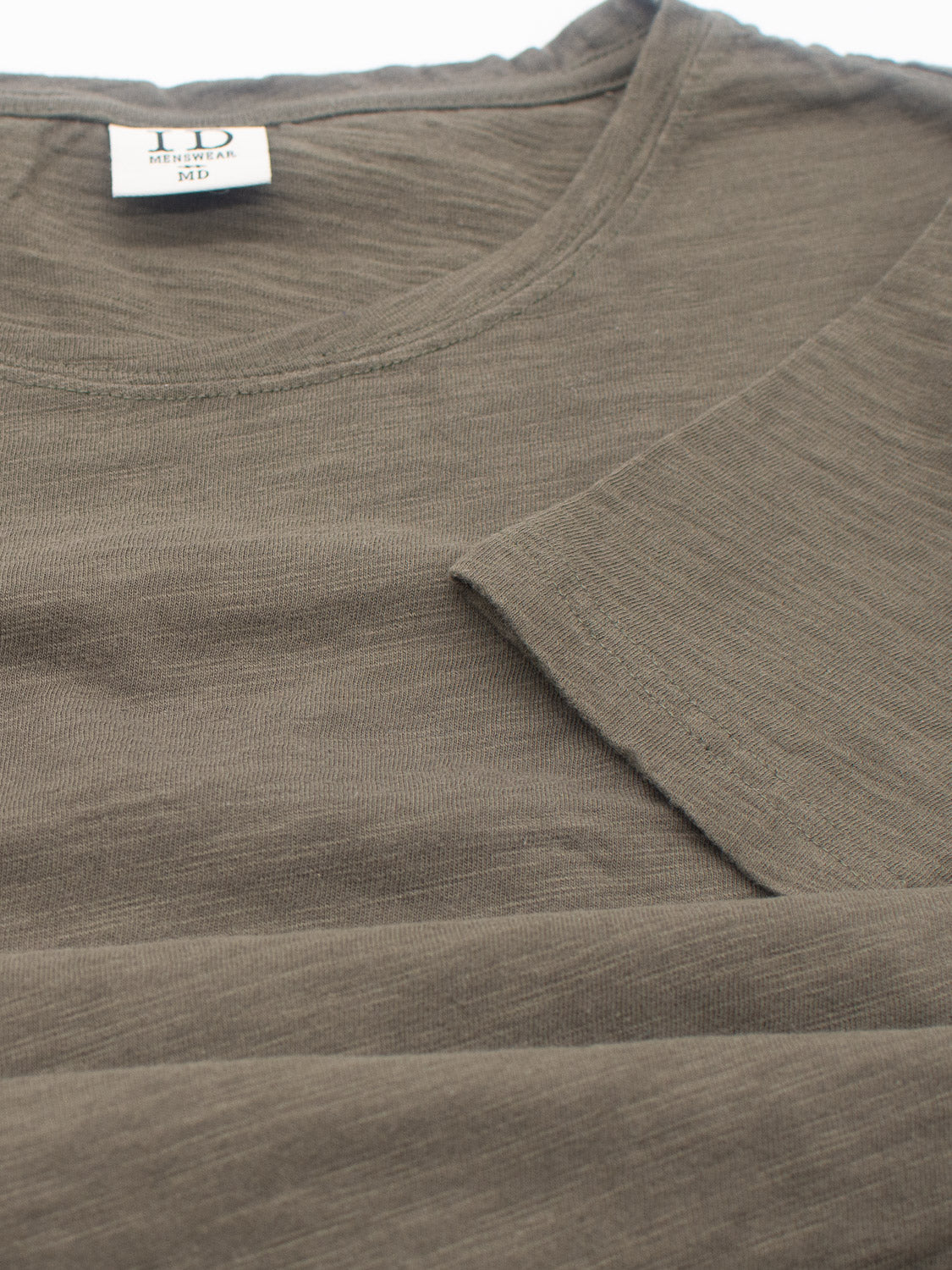 The Mini Flip Slub Yarn Tee by ID Menswear is shown in a close-up view. This soft, lightweight sage green T-shirt, ideal for everyday wear, features a round neckline, folded sleeve, and visible clothing label at the neck. Made from textured slub cotton.