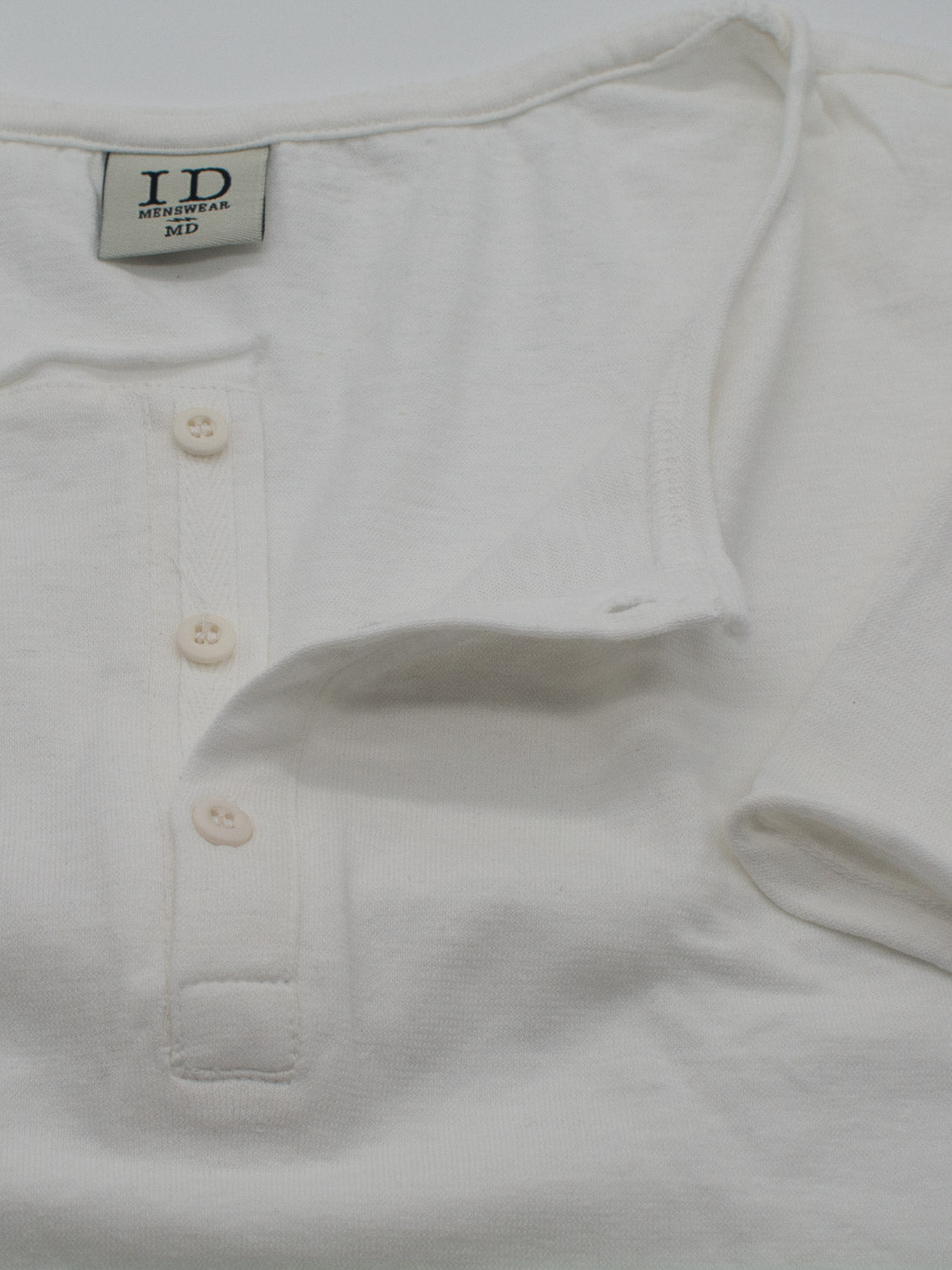 Close-up of the Legend Hemp Cotton Rolled Neck Henley in soft, organic cotton, featuring a tag labeled ID Menswear. This breathable shirt has three buttons on the placket and short sleeves.
