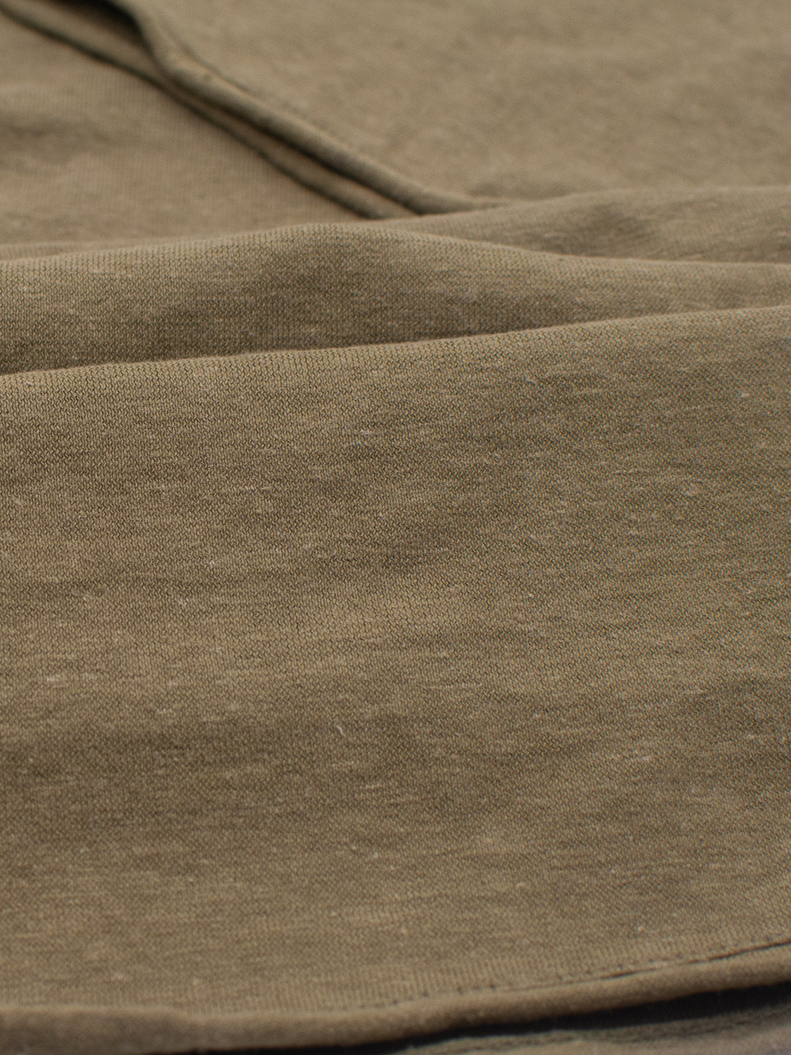 Close-up of the soft, textured fabric from ID Menswears Legend Hemp Cotton Rolled Neck Henley in olive green, showcasing visible weaves and folds that form a gentle, wavy pattern.
