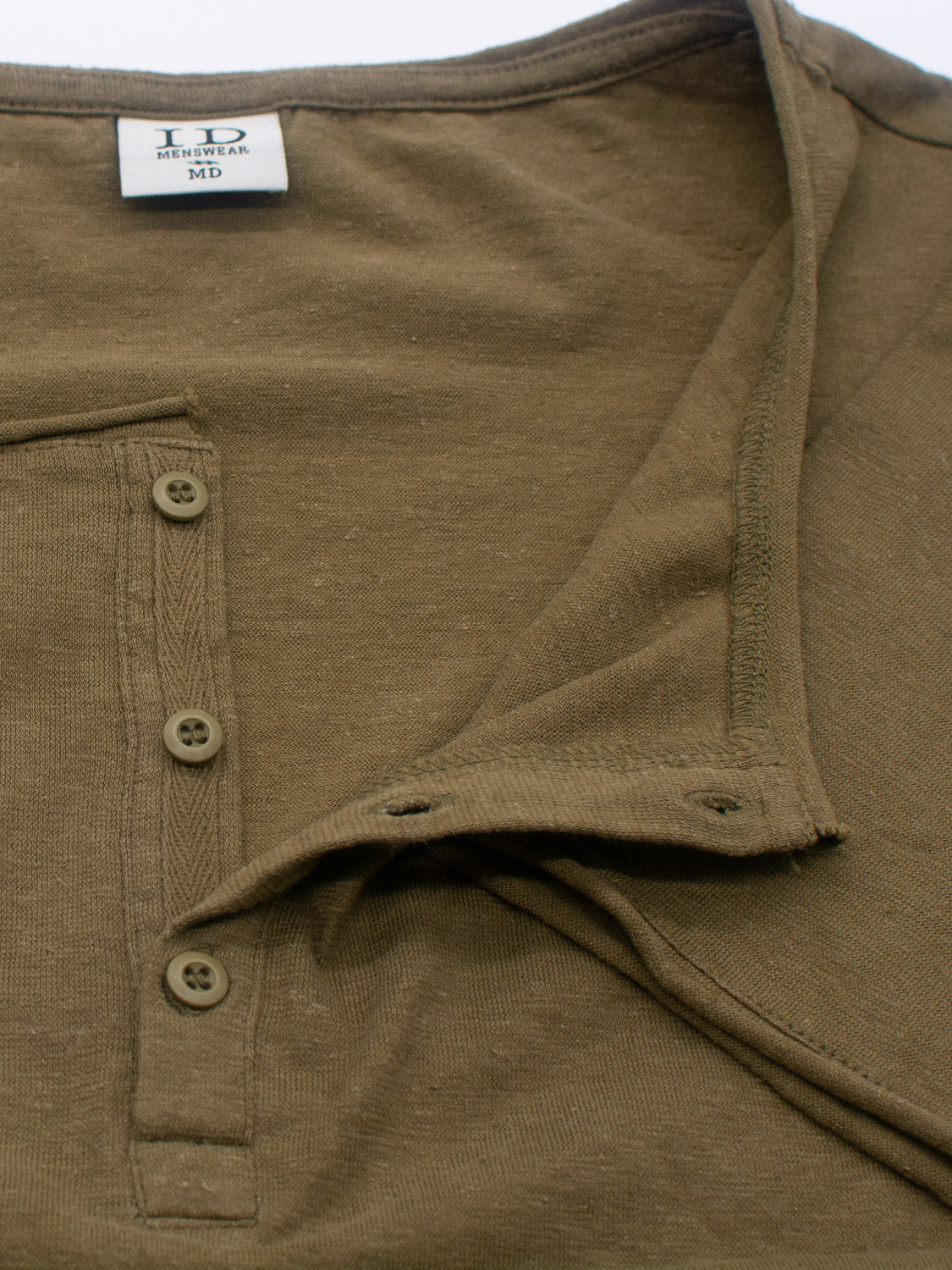 Close-up of the olive-green Legend Hemp Cotton Rolled Neck Henley by ID Menswear, highlighting its breathable hemp texture and unbuttoned placket. A small stitched label near the collar displays ID, NEW WEAR, MD.