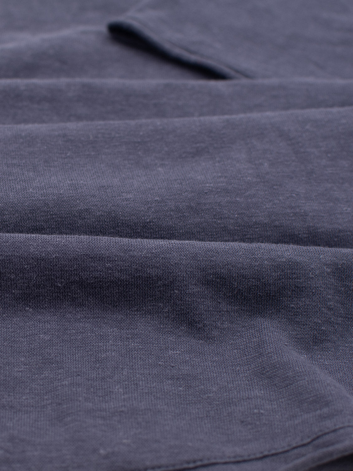 A close-up of navy fabric from the Legend Hemp Cotton Rolled Neck Henley by ID Menswear reveals its soft, smooth texture with subtle highlights and shadows, accentuating its contours.