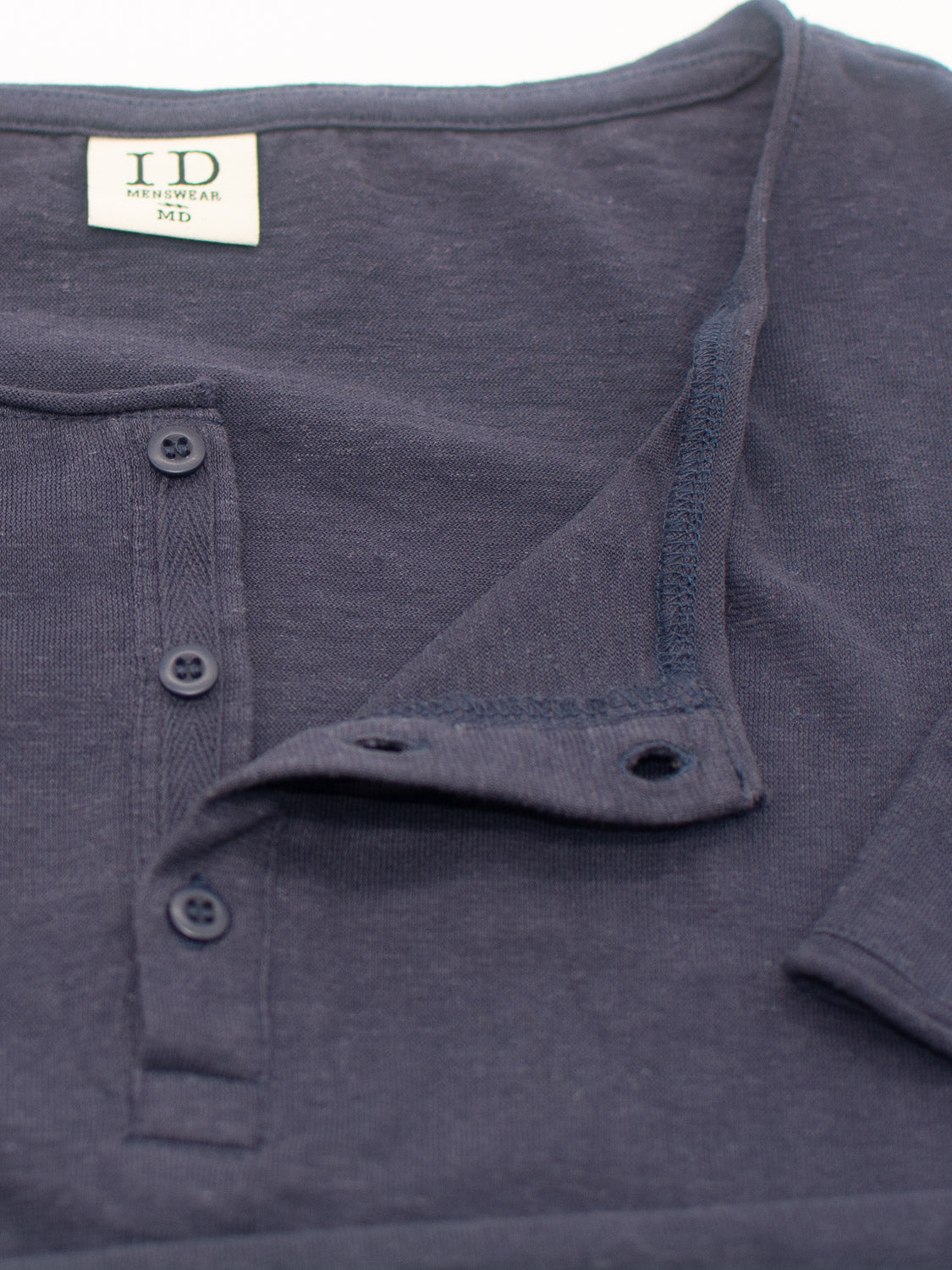 The Legend Hemp Cotton Rolled Neck Henley by ID Menswear is a dark gray, breathable shirt made from organic cotton. It has a partially open placket with three black buttons and displays the ID MENSWEAR and MD label in black text on a white background.