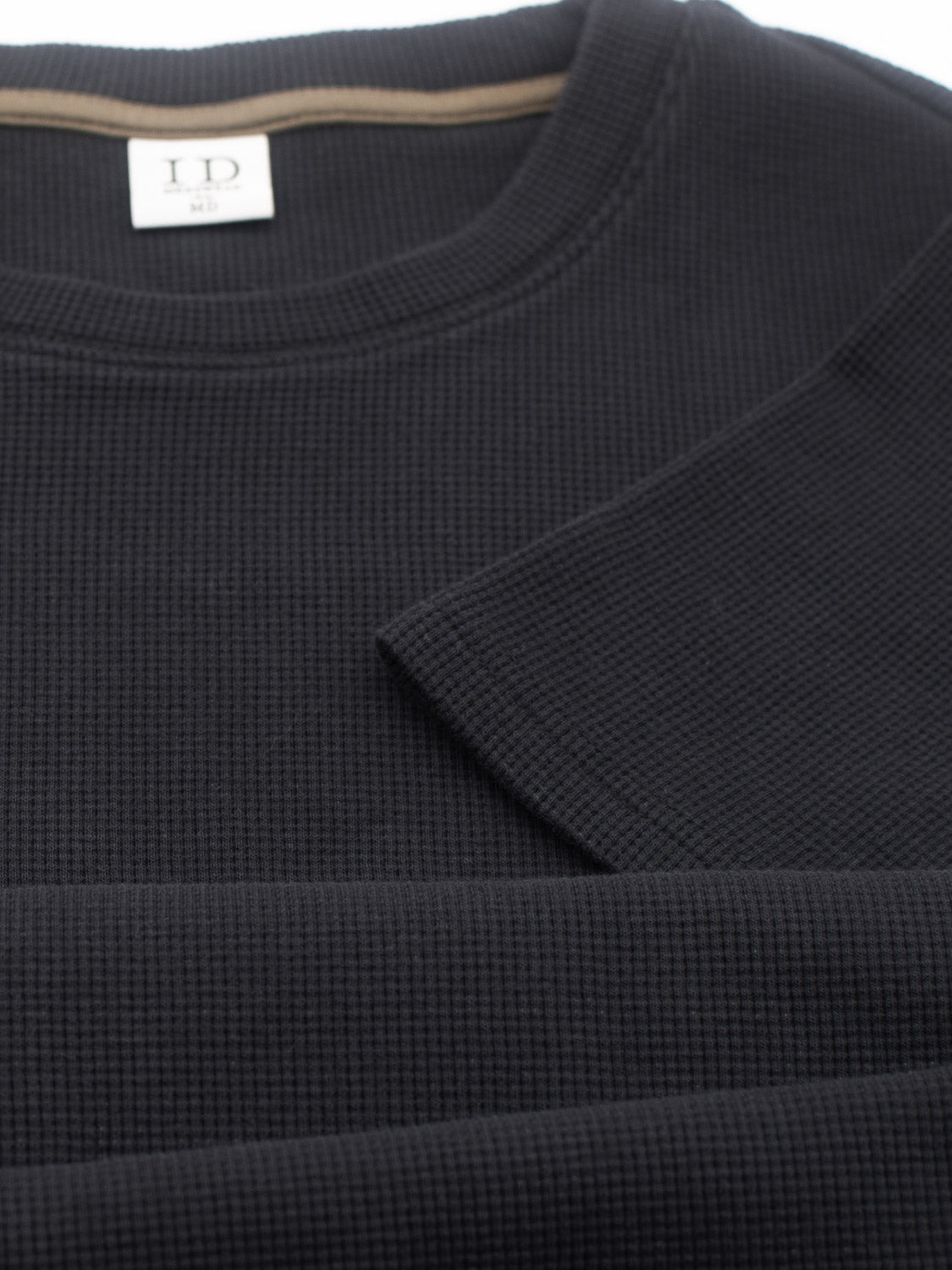 Close-up of the Urban Waffle Knit Tee from ID Menswear, neatly folded to highlight its texture and stitching. Made from a comfy cotton-spandex blend, it features a white label at the collar reading ID M and is set against a neutral background.