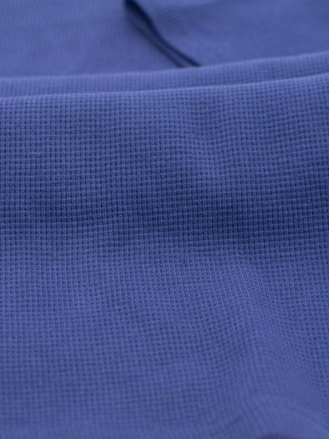 Close-up of the Urban Waffle Knit Tee by ID Menswear, featuring a blue waffle-knit fabric with tiny, raised squares. The cotton-spandex blend has a smooth surface and soft folds, making it ideal for casual wear.