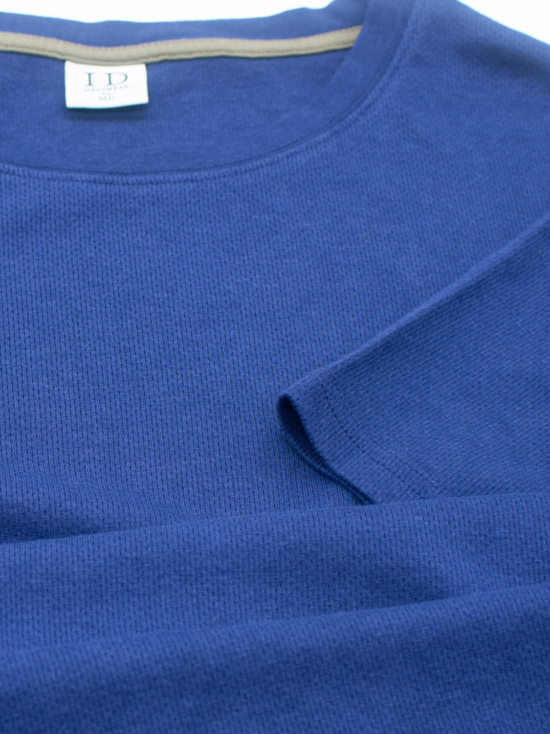 Close-up of the Urban Honeycomb Mesh Tee by ID Menswear, laid flat in blue. Crafted from a bamboo-organic cotton blend, it reveals the neckline with a label, and part of a sleeve is visible. The textured fabric offers breathable comfort.