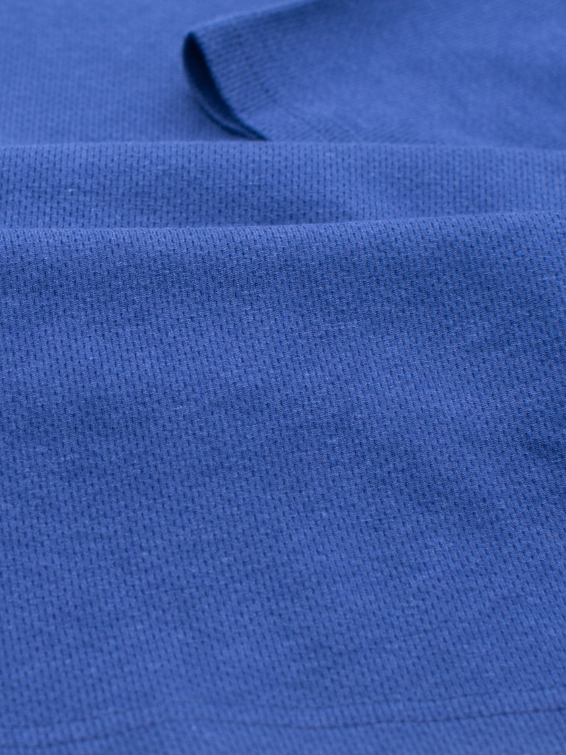 Close-up of a textured blue Urban Honeycomb Mesh Tee by ID Menswear, displaying its grid-like pattern and breathable texture. The bamboo-organic cotton blend gently folds into small waves and shadows.