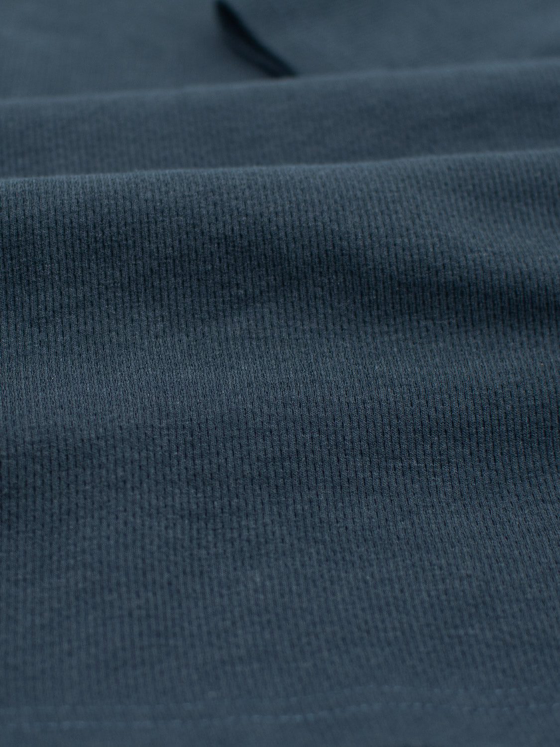 Close-up of the Urban Honeycomb Mesh Tee by ID Menswear, showcasing its textured dark green bamboo-organic cotton blend. The fabric features a subtle ribbed pattern that adds depth and interest, highlighting the smooth surface and intricate details.