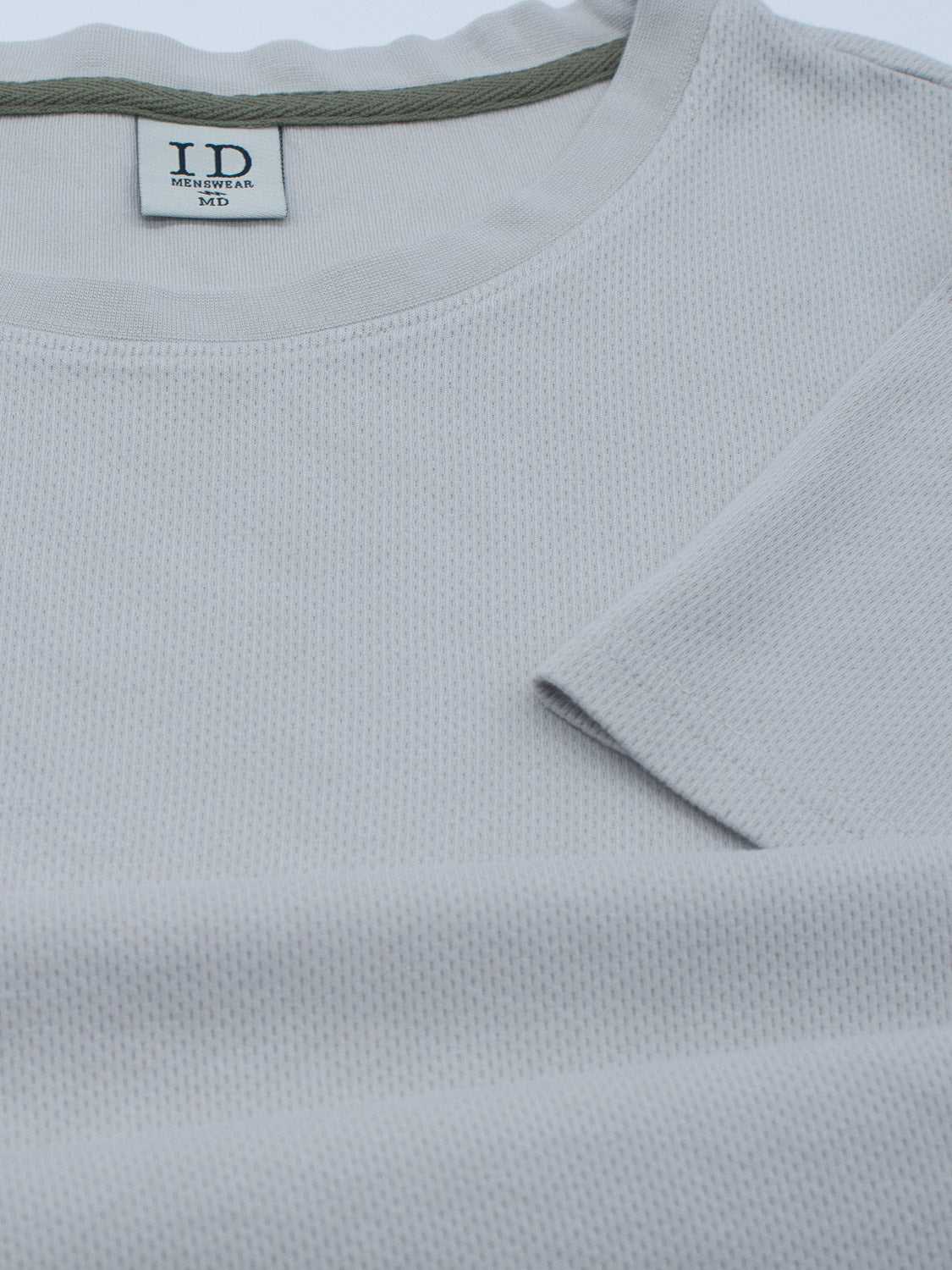 A close-up of the Urban Honeycomb Mesh Tee in light gray from ID Menswear, showcasing its breathable bamboo-organic cotton blend and round neckline. The label reads ID, Medium. Laid flat minimalistically, it highlights the tees soft and airy feel.
