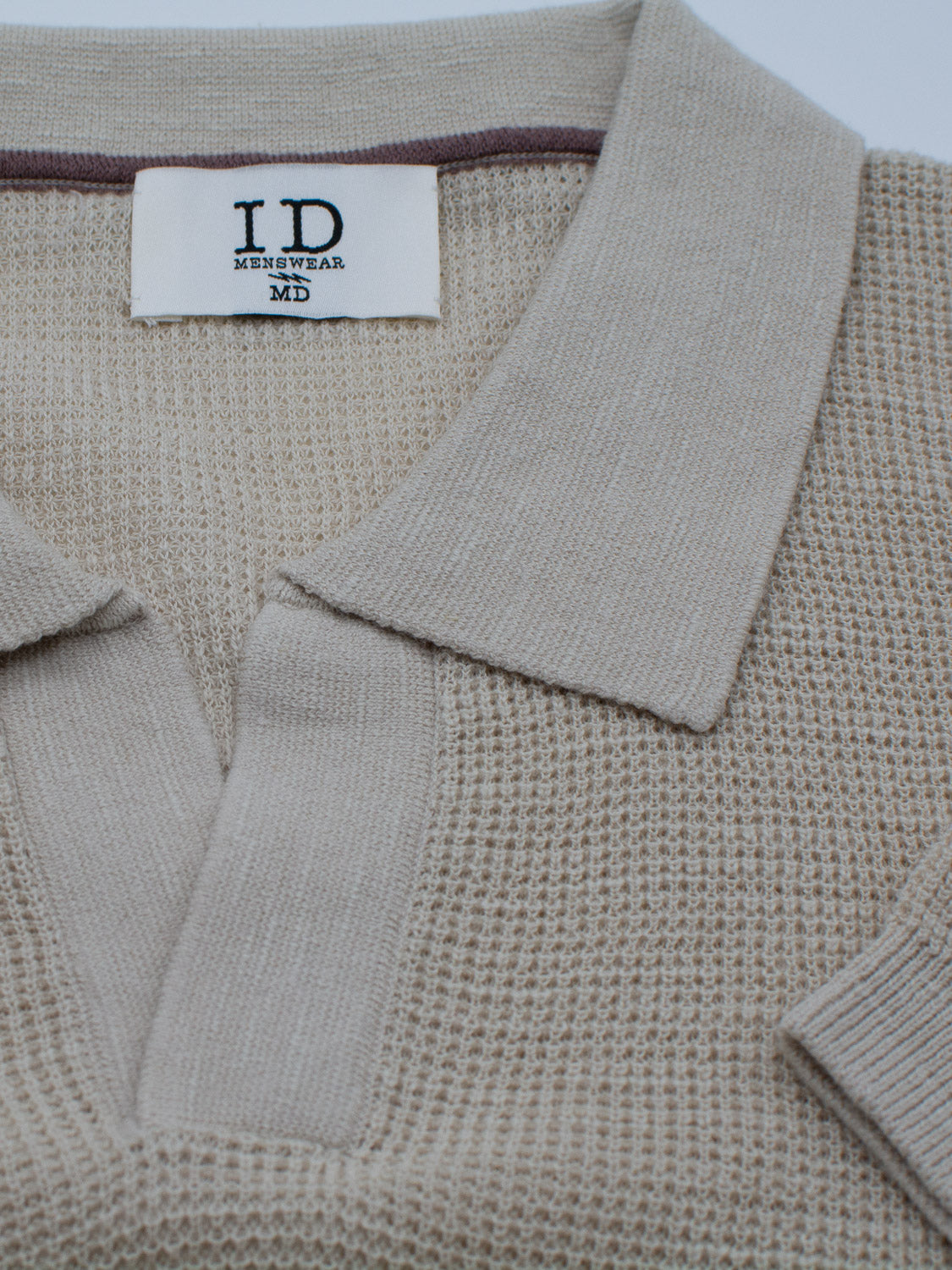 Close-up of the Ankara Linen Blend Waffle Knit Polo in beige, with a textured pattern and fold-over collar. Lightweight and breathable, perfect for warm weather. The inside neckline shows a label reading ID Menswear MD against a plain background.