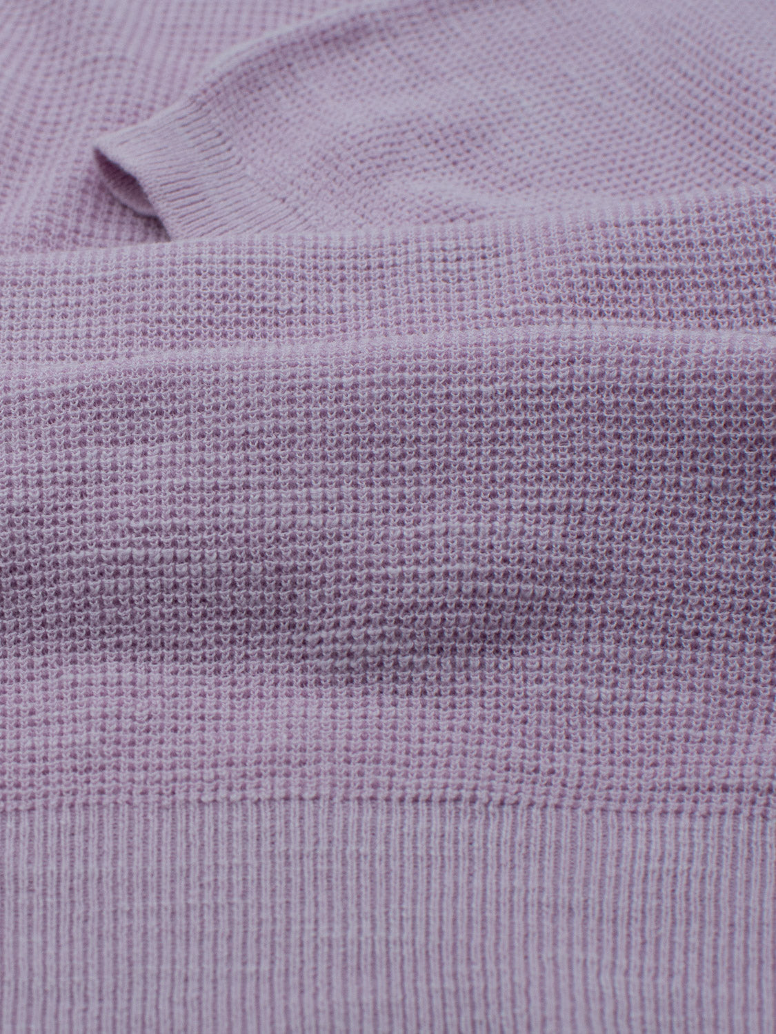 Close-up of the Ankara Linen Blend Waffle Knit Polo by ID Menswear, crafted from lightweight lavender fabric with a textured pattern. Soft and slightly heathered, it features subtle tone variations for warmth and coziness—perfect for warm weather.