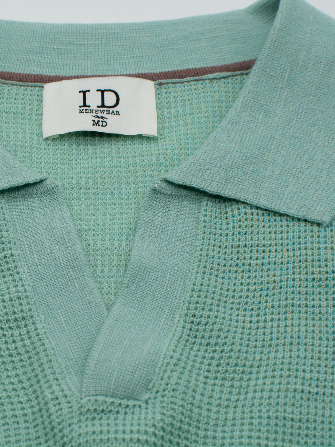 Close-up of the Ankara Linen Blend Waffle Knit Polo in light green by ID Menswear, featuring a collar and partially open placket. The neckline label reads ID Menswear MD with a brown-striped edge—perfect for warm weather.