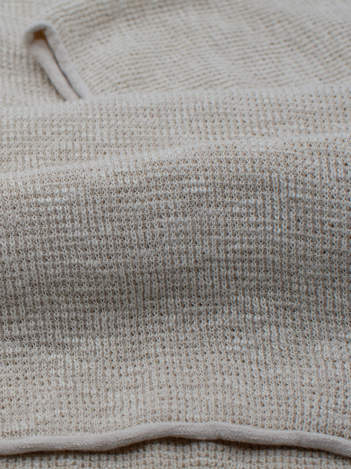 Close-up of the Athens Waffle Knit Polo by ID Menswear in textured beige fabric, resembling a waffle-knit pattern. The casual style shows in its soft, looped surface with gentle folds creating shadows and contours. Edges at the top and bottom enhance the textured look.