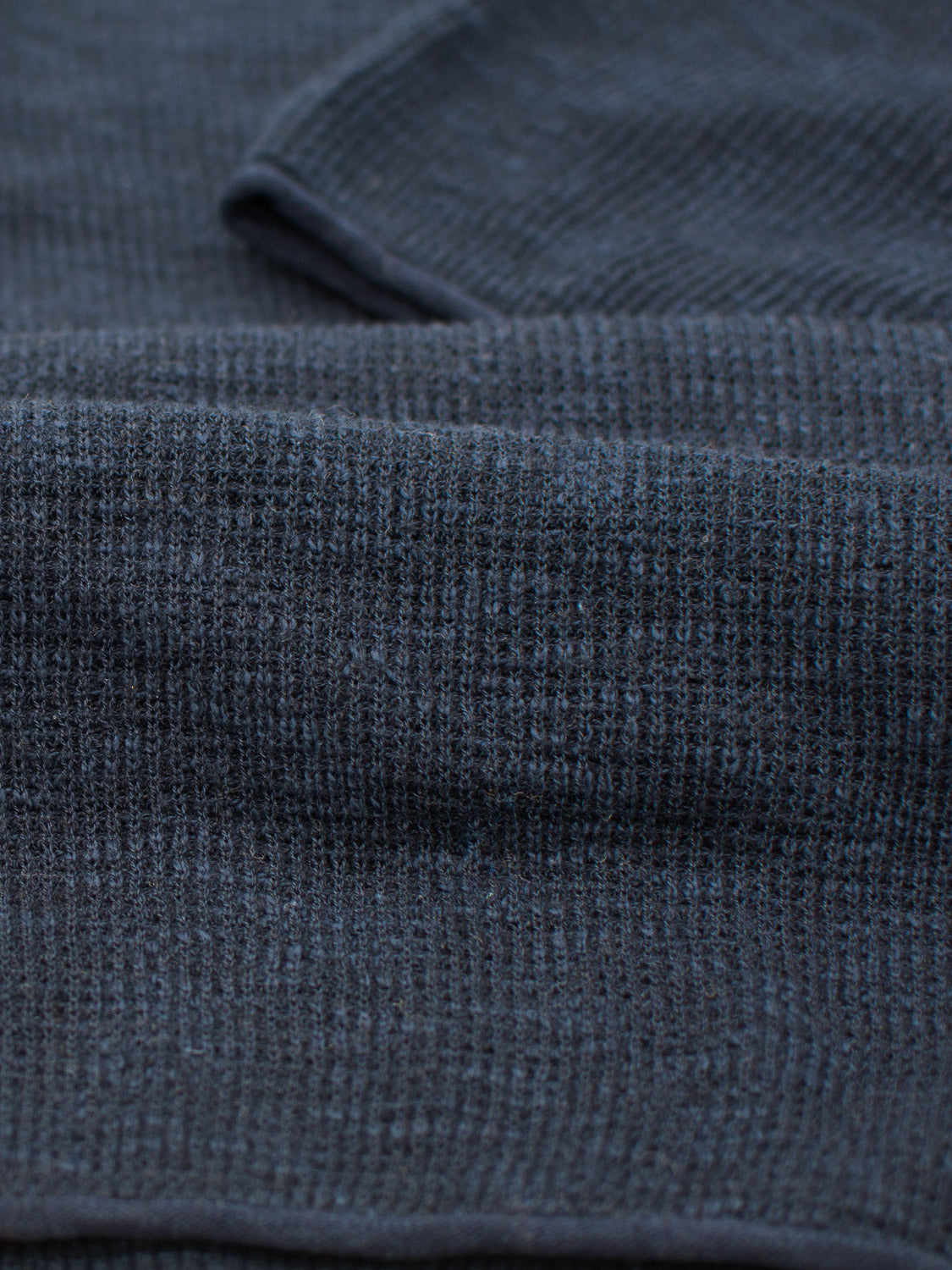 A close-up of the folded Athens Waffle Knit Polo by ID Menswear shows a gray, textured fabric with a waffle weave, offering a casual style. The material appears soft and plush, suggesting a cozy and warm textile with a textured look.