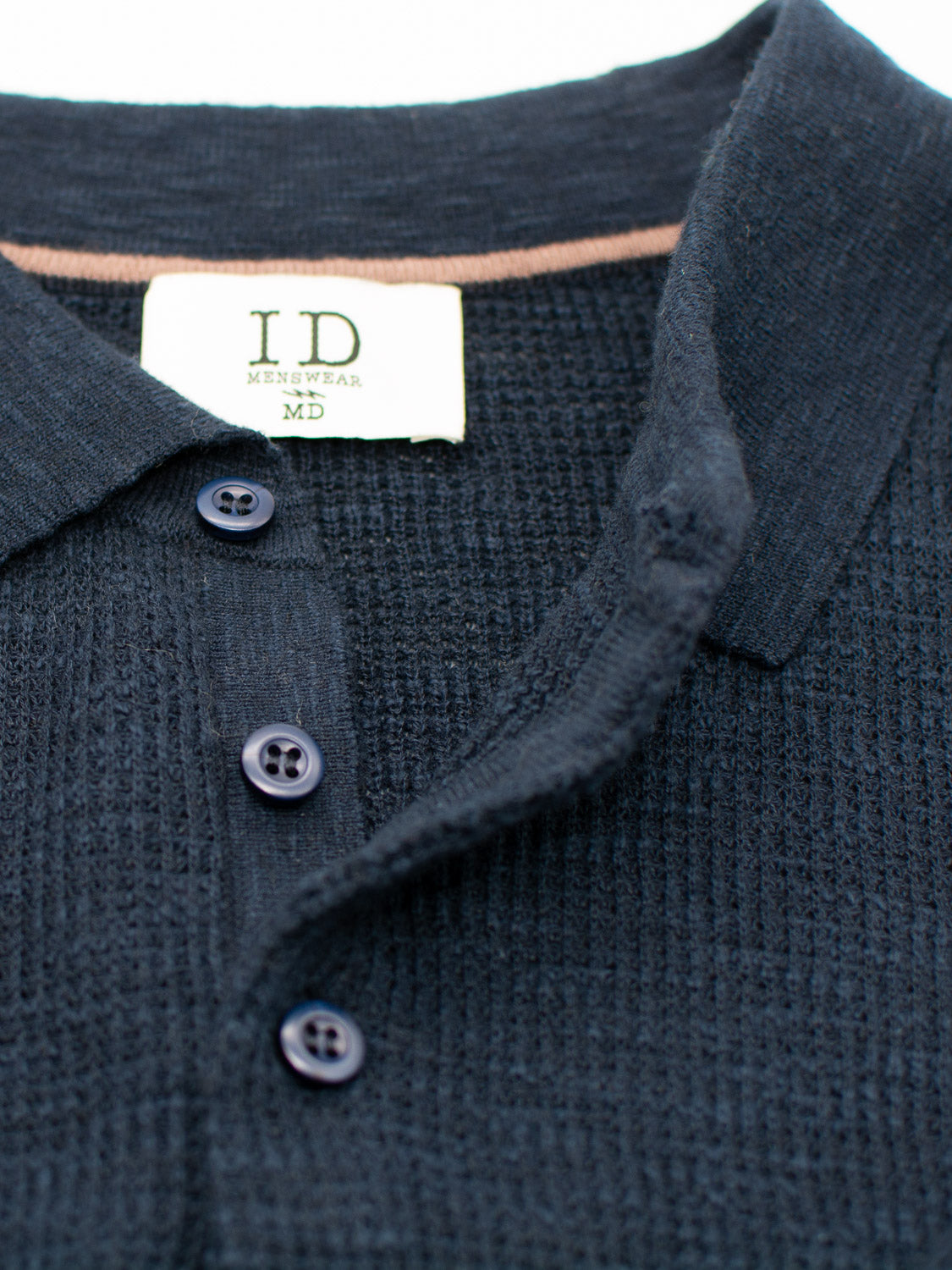 Close-up of a dark Athens Waffle Knit Polo by ID Menswear, featuring a collar, three dark buttons, and an ID Menswear MD label at the neck. The textured fabric enhances its unique blend of casual style and sophistication.