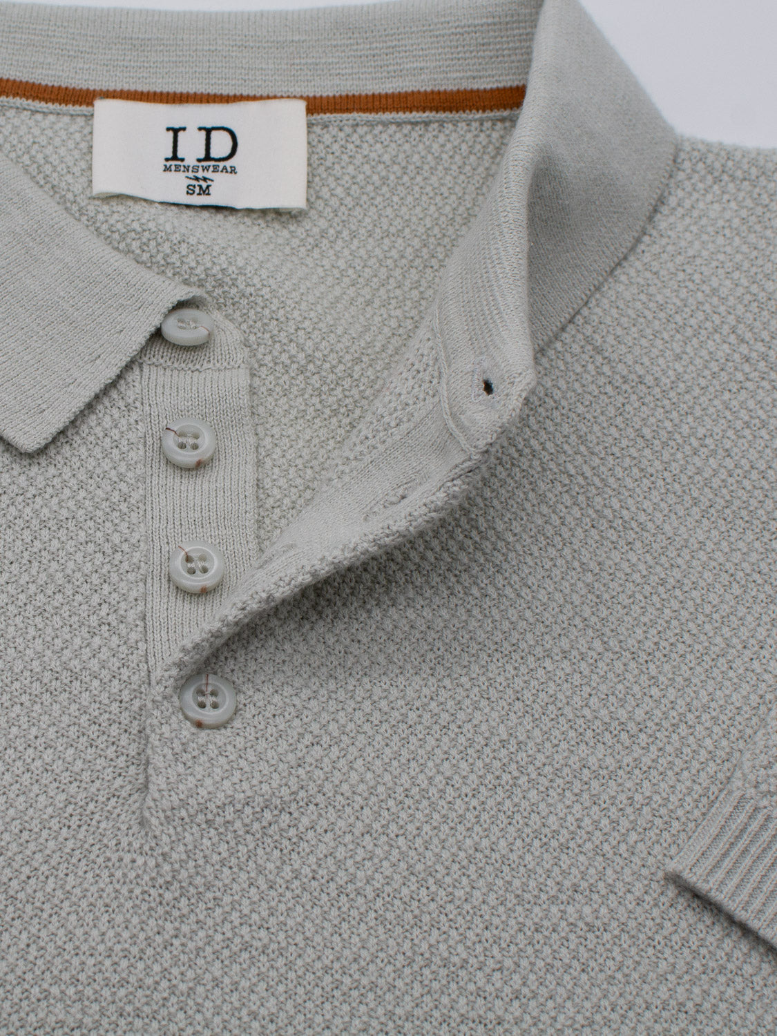 The close-up shows the Austin Knitted Cotton Polo by ID Menswear, featuring a textured grey design with a breathable fit, short collar, and three-button placket. A label inside reads ID Menswear SM.