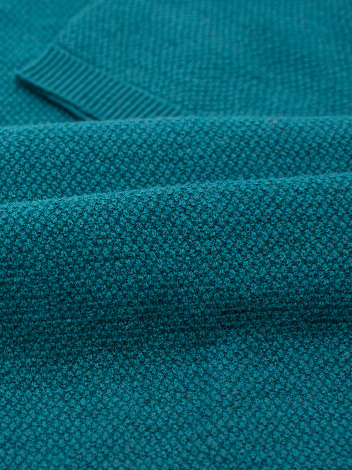 Close-up of the Austin Knitted Cotton Polo by ID Menswear, showcasing its teal knit fabric with a textured pattern. The image captures the woven structure, rich color, and breathable fit with folds that create varying shades and depths, ideal for casual wear.
