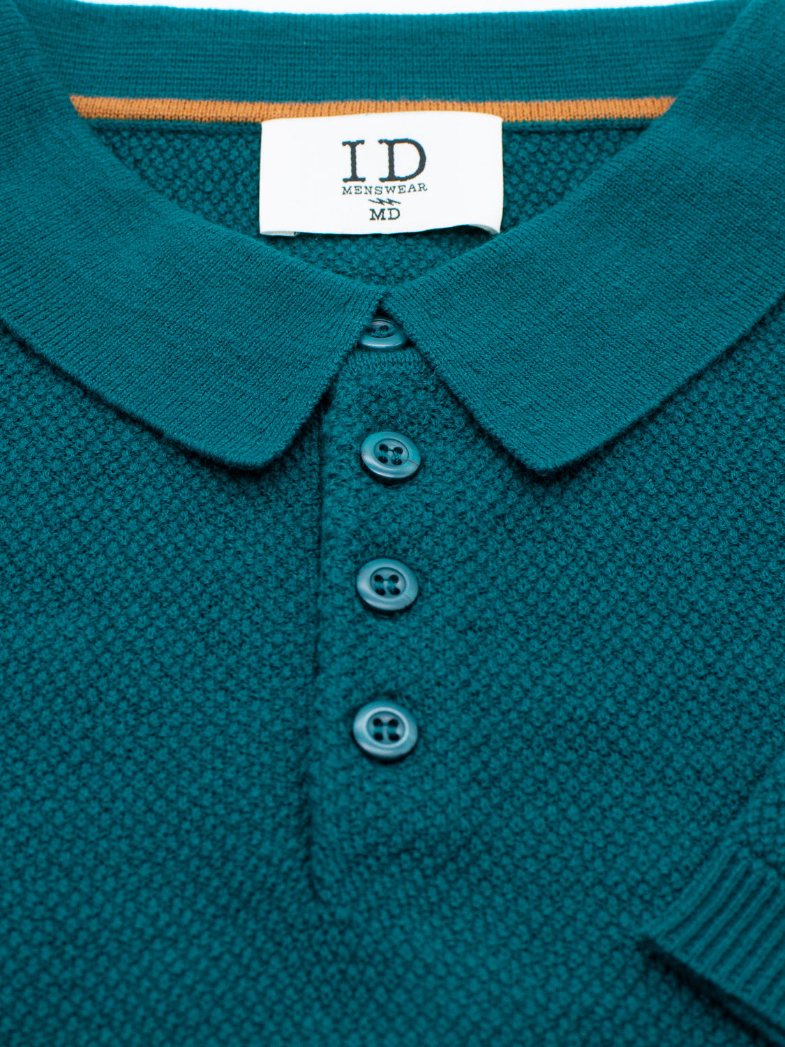 Close-up of the Austin Knitted Cotton Polo by ID Menswear, featuring a teal textured design, folded collar, and four matching buttons. Perfect for casual wear with its breathable cotton-knit fit. A white label inside the collar reads ID Menswear MD.