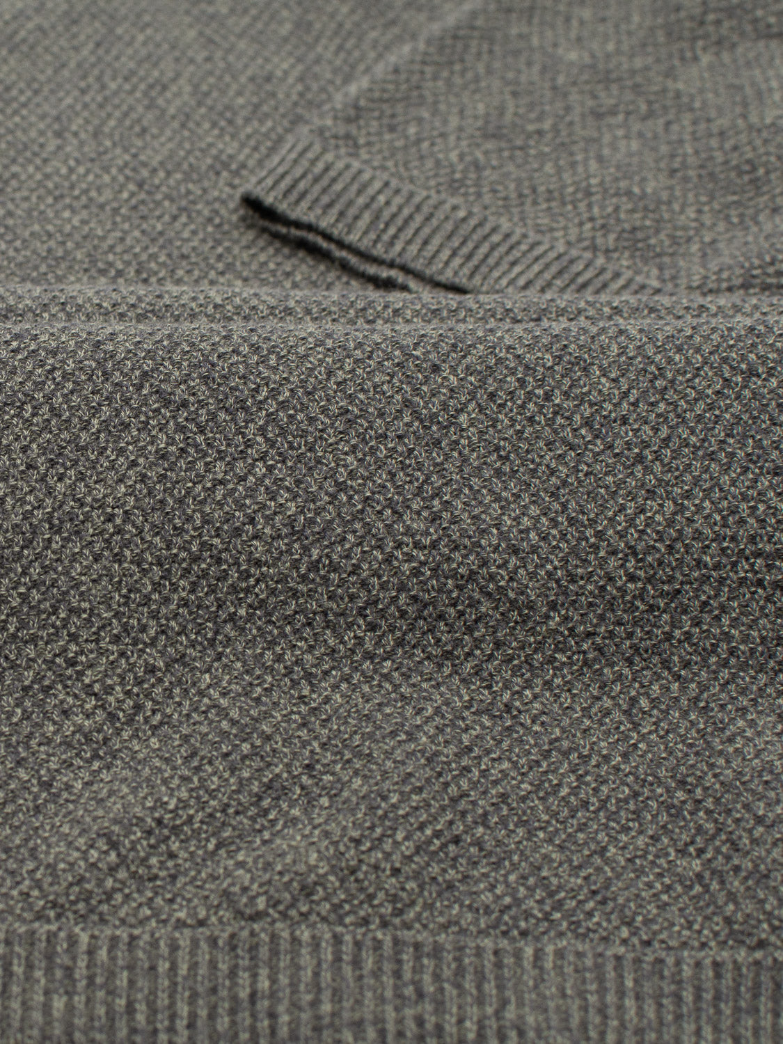 A close-up of ID Menswears Austin Knitted Cotton Polo reveals a soft, lightweight gray fabric with a subtle herringbone pattern. Its ribbed edges enhance casual style, reminiscent of polo or cardigan designs, while ensuring breathable comfort for everyday wear.