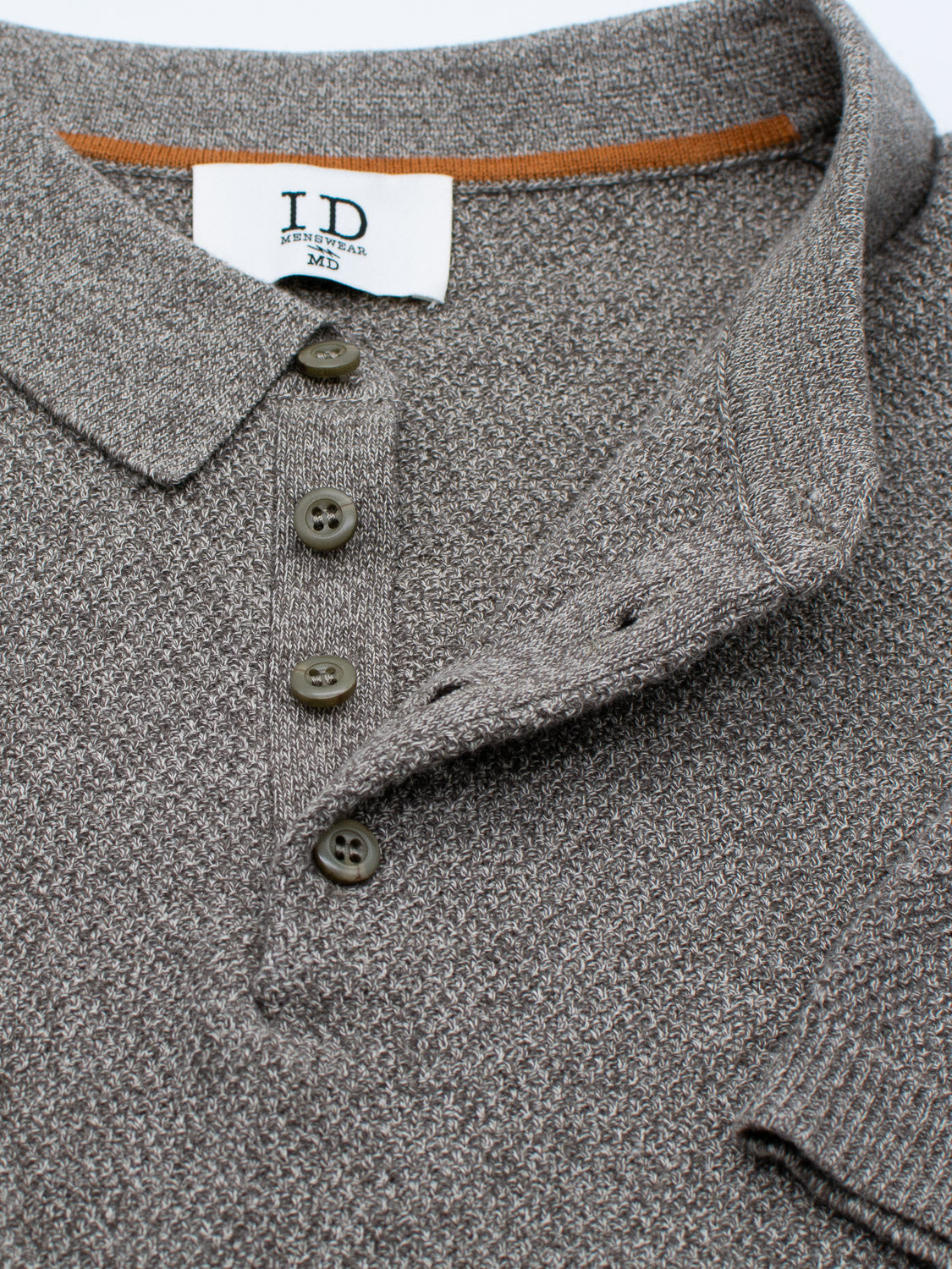 The Austin Knitted Cotton Polo from ID Menswear features a textured brown knit with a folded collar and three dark buttons for a breathable fit. Inside the collar, the label reads ID Menswear, ATHLEISUREWEAR, M. Ideal for casual attire.