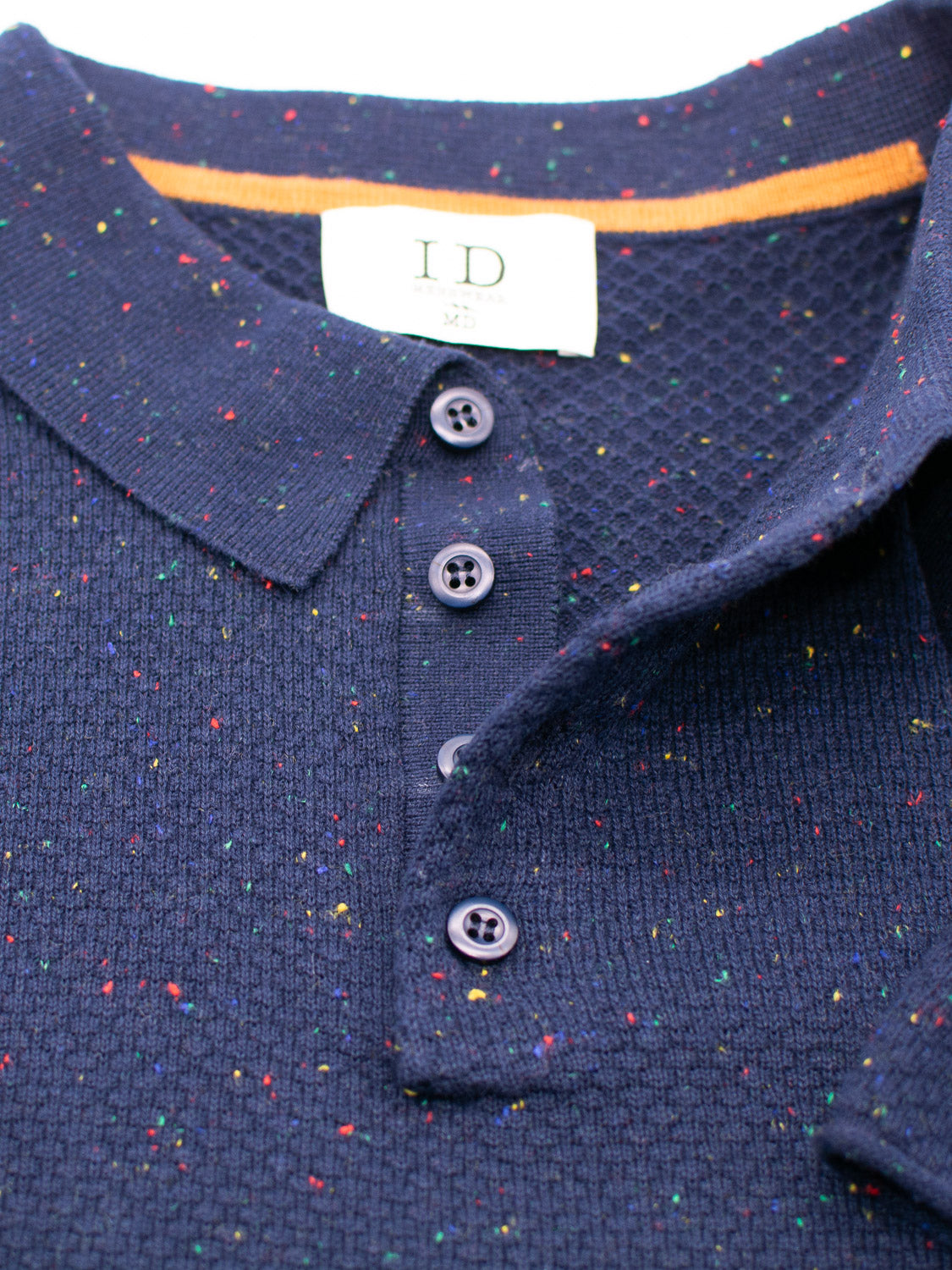 The Denver Speckled Knit Cotton Polo by ID Menswear is navy blue with a multicolored speckled pattern, buttoned up with three dark buttons. It has a textured, breathable fit and orange trim inside the collar with a visible white label, ideal for casual wear.