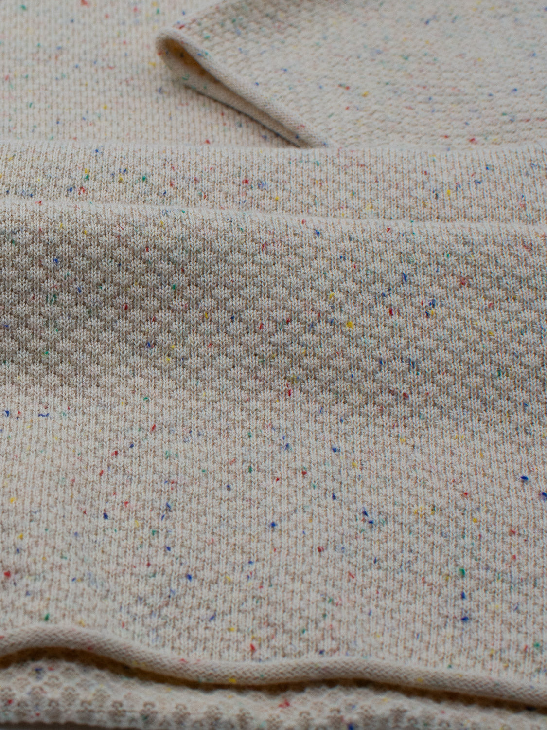 Close-up of ID Menswears Denver Speckled Knit Cotton Polo, showcasing cream-colored textured fabric with colorful specks in blue, yellow, red, and green. Perfect for casual wear with a soft, breathable fit and knitted surface.