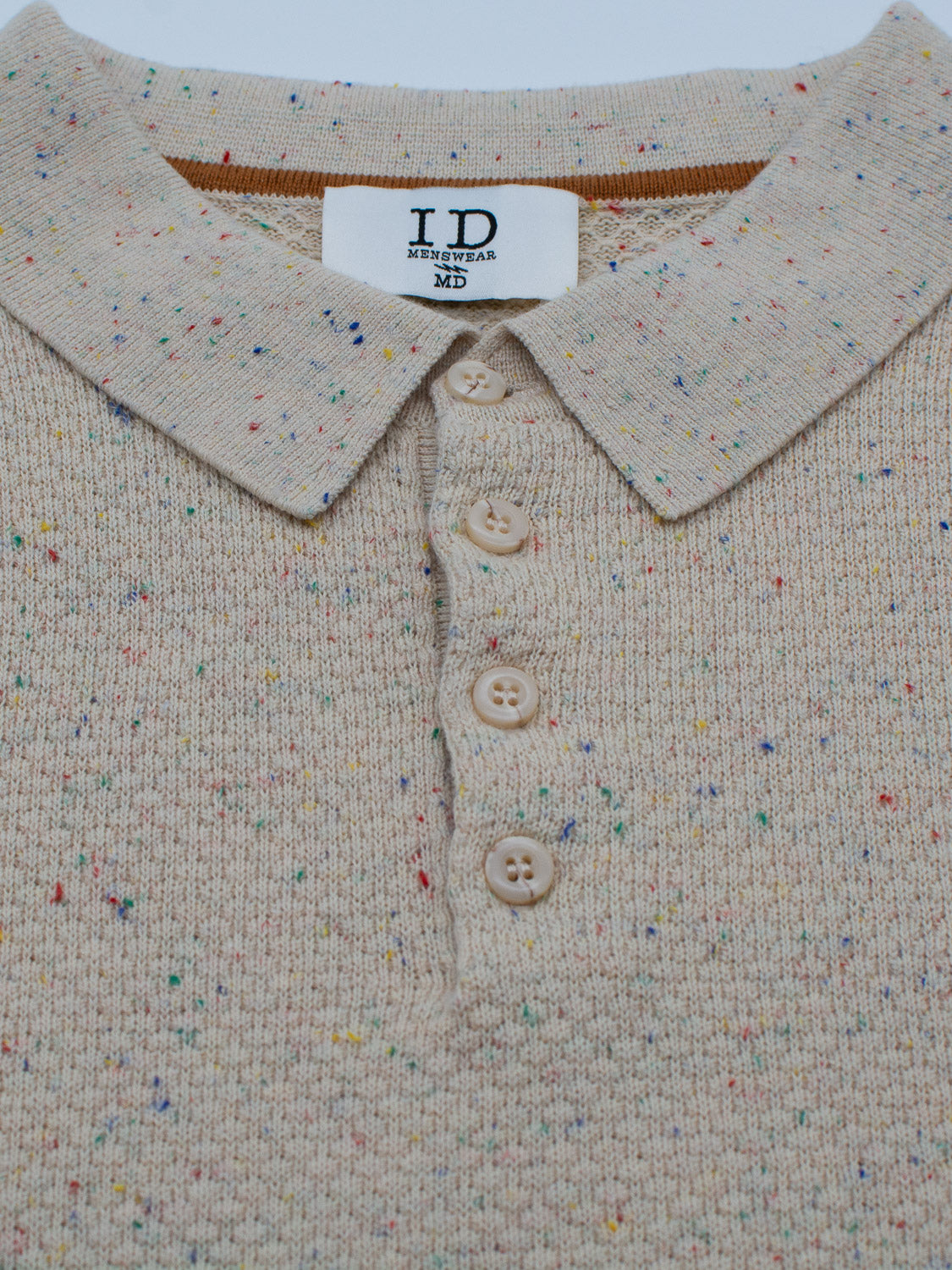 Close-up of the Denver Speckled Knit Cotton Polo by ID Menswear: a beige knit polo with a collar, four beige buttons, and multicolored specks across its breathable 100% cotton fabric. Perfect for casual wear and reflects quality craftsmanship.