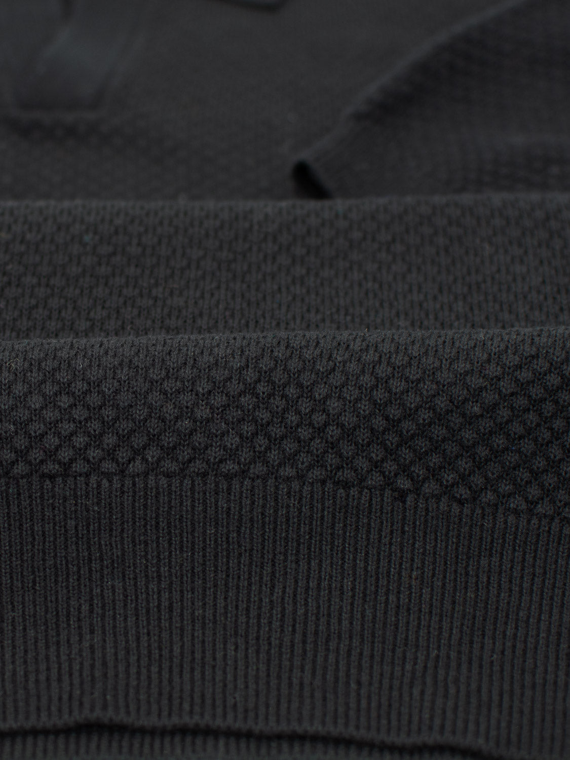 The Malaga Knitted Cotton Polo by ID Menswear features a close-up of its dark, textured fabric with intricate, ribbed horizontal lines. Made from 100% cotton in a dark gray or black hue, it showcases timeless elegance and depth.