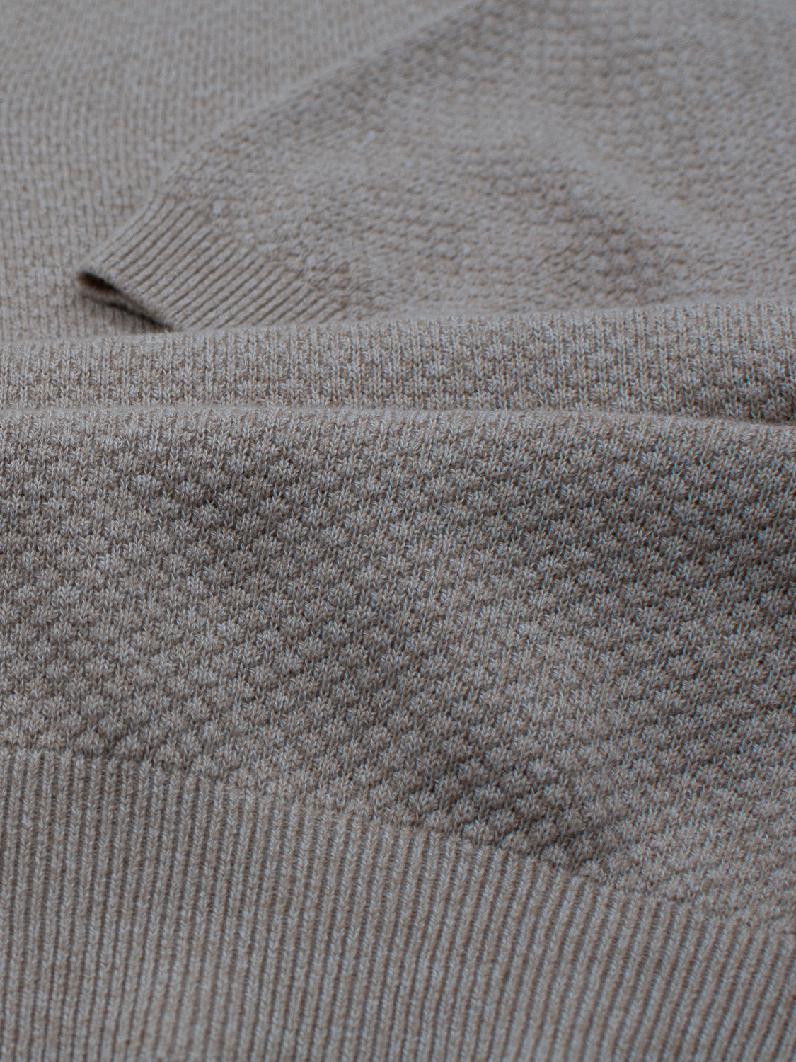 Close-up of a folded gray knitted textile from ID Menswears Malaga Knitted Cotton Polo, exuding timeless elegance with a detailed texture. Made from 100% cotton, it features a ribbed edge at the bottom that contrasts subtly with the smoother sections.