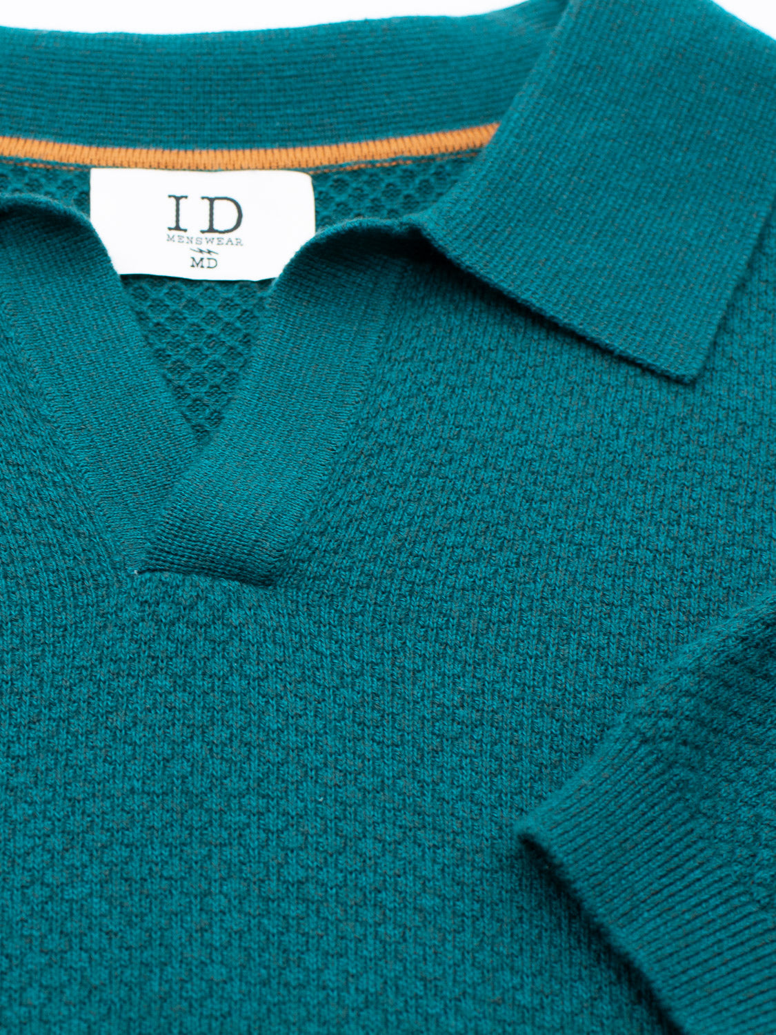 Close-up of a timeless Malaga Knitted Cotton Polo in teal, featuring a collar and V-neck. The ID Menswear label inside notes menswear sizing, marked M and D. A hint of orange inner lining at the collar enhances its sophisticated charm.