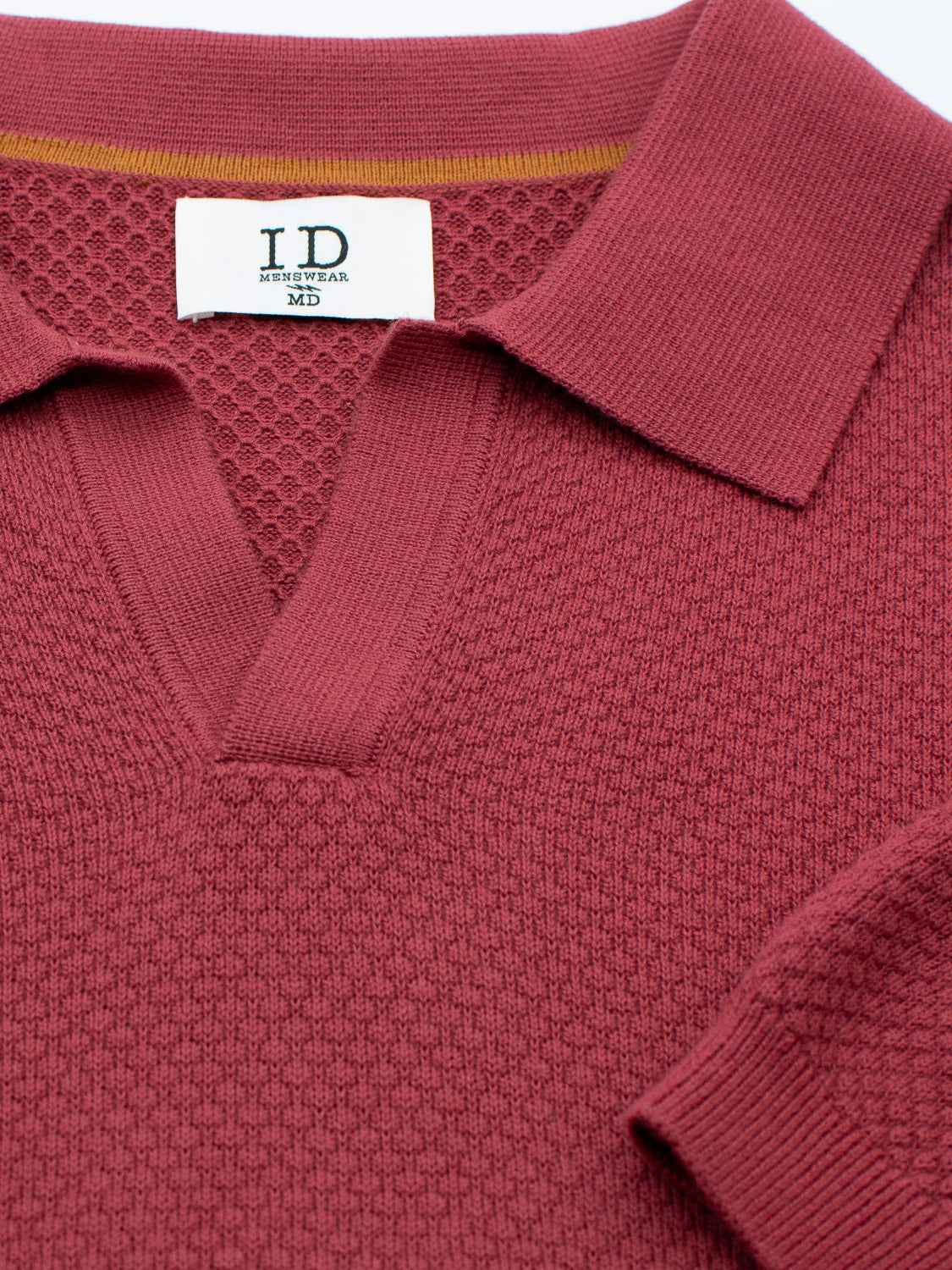 Close-up of a red, textured knit Malaga Knitted Cotton Polo with a partially open collar displays the ID Menswear label inside. Made from 100% cotton, its distinct weave pattern adds timeless elegance and depth to the garment.