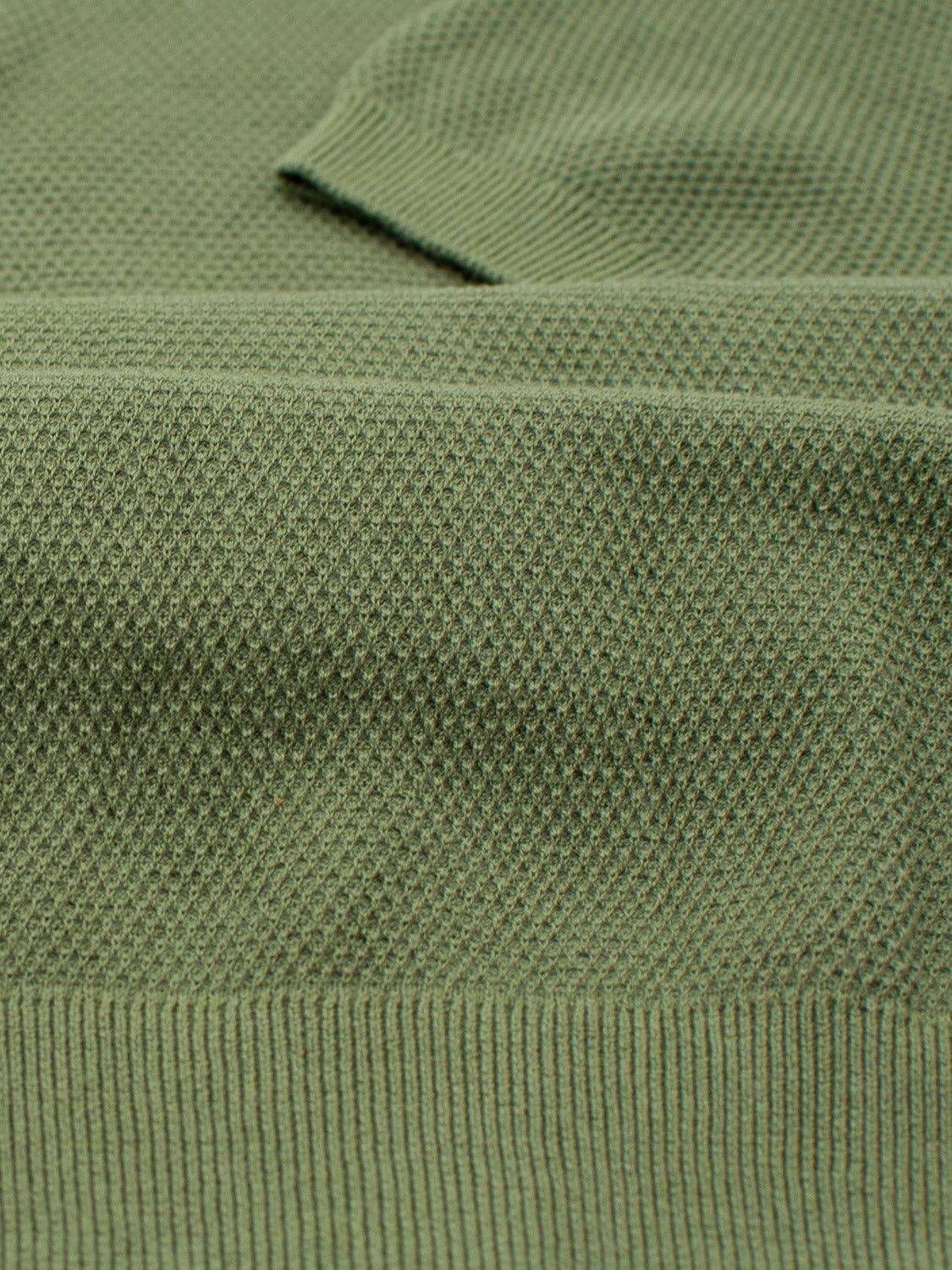 A close-up of the Monaco Knitted Cotton Polo by ID Menswear shows its textured green fabric with a ribbed hem, intricately woven from 100% cotton for ultimate comfort.