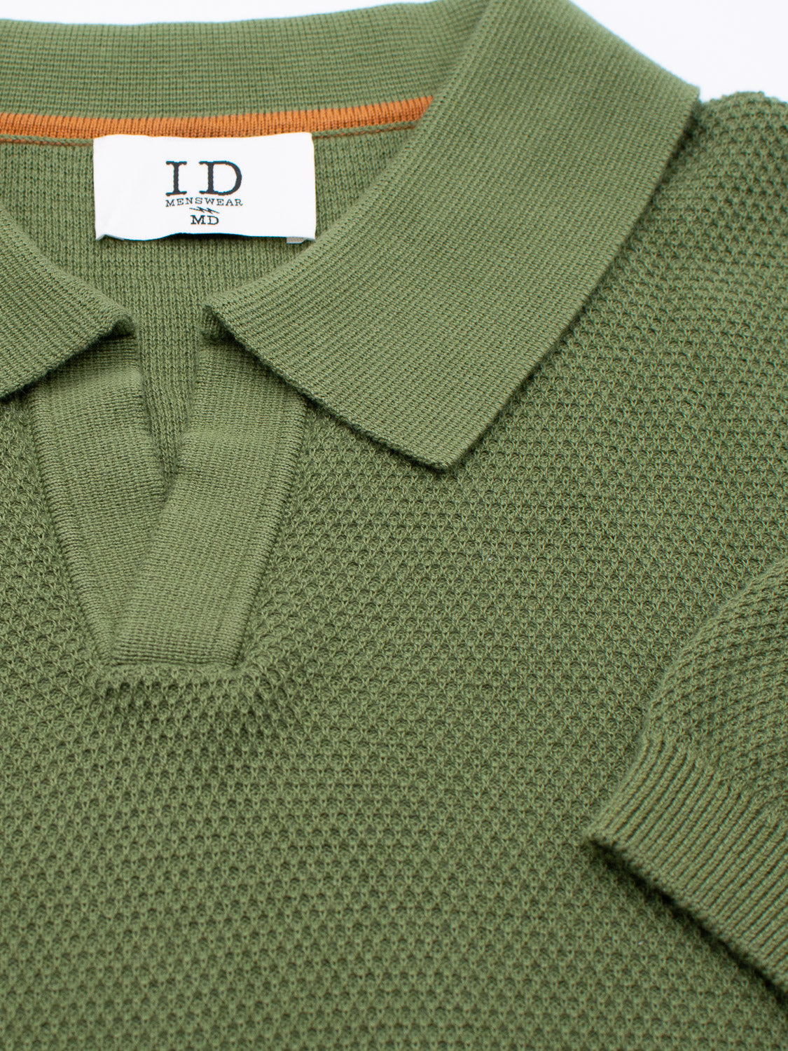 Close-up of a green Monaco Knitted Cotton Polo by ID Menswear, made from 100% cotton. It features a folded collar, a small orange stripe inside the neckline, and an inner white label that reads I.D, MENSWEAR, MD.