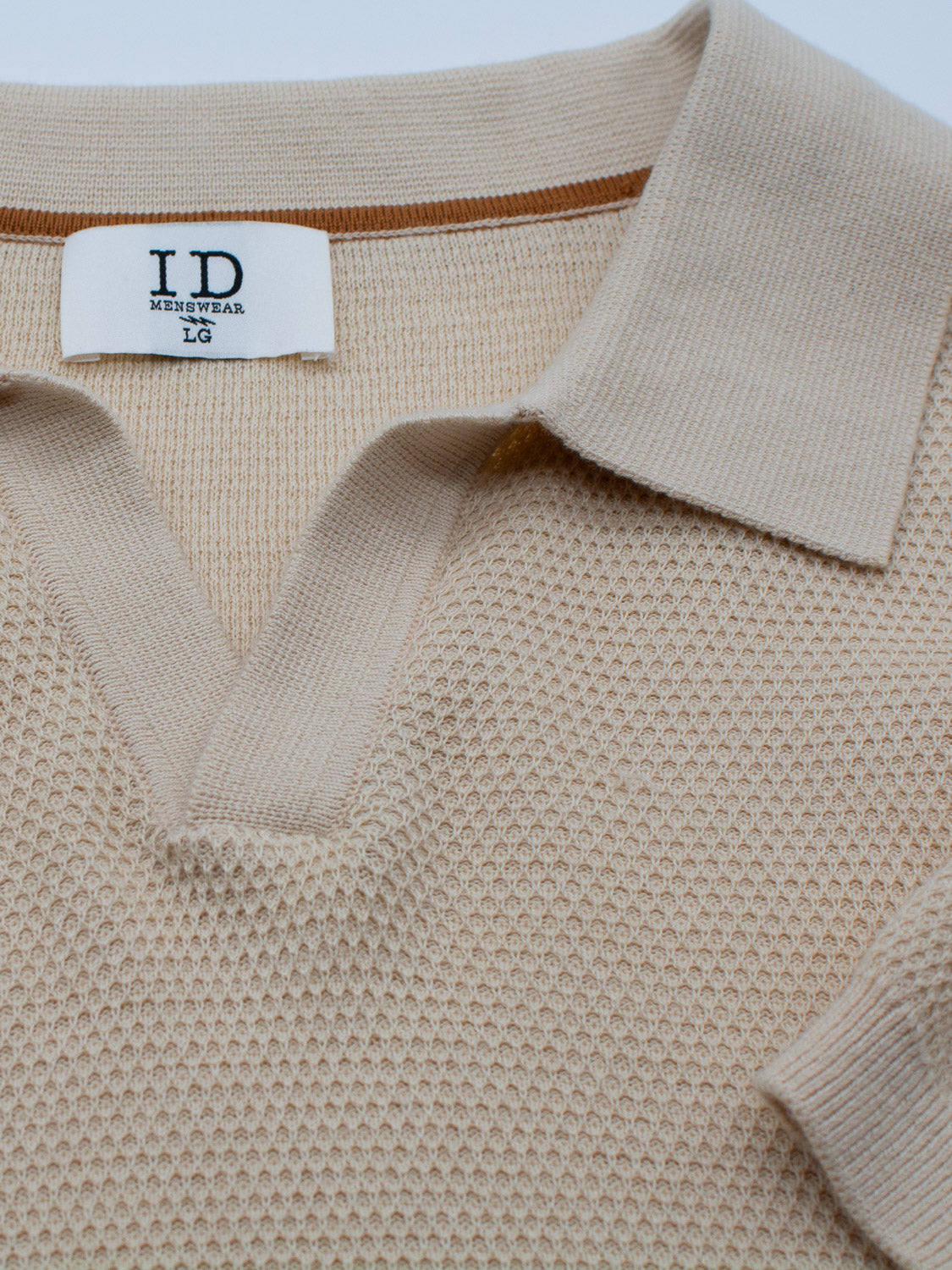 Close-up of the Monaco Knitted Cotton Polo by ID Menswear, a beige textured lightweight shirt crafted from 100% cotton. It features a collar and open neckline with an LG size tag. The fabric pattern is neatly showcased.